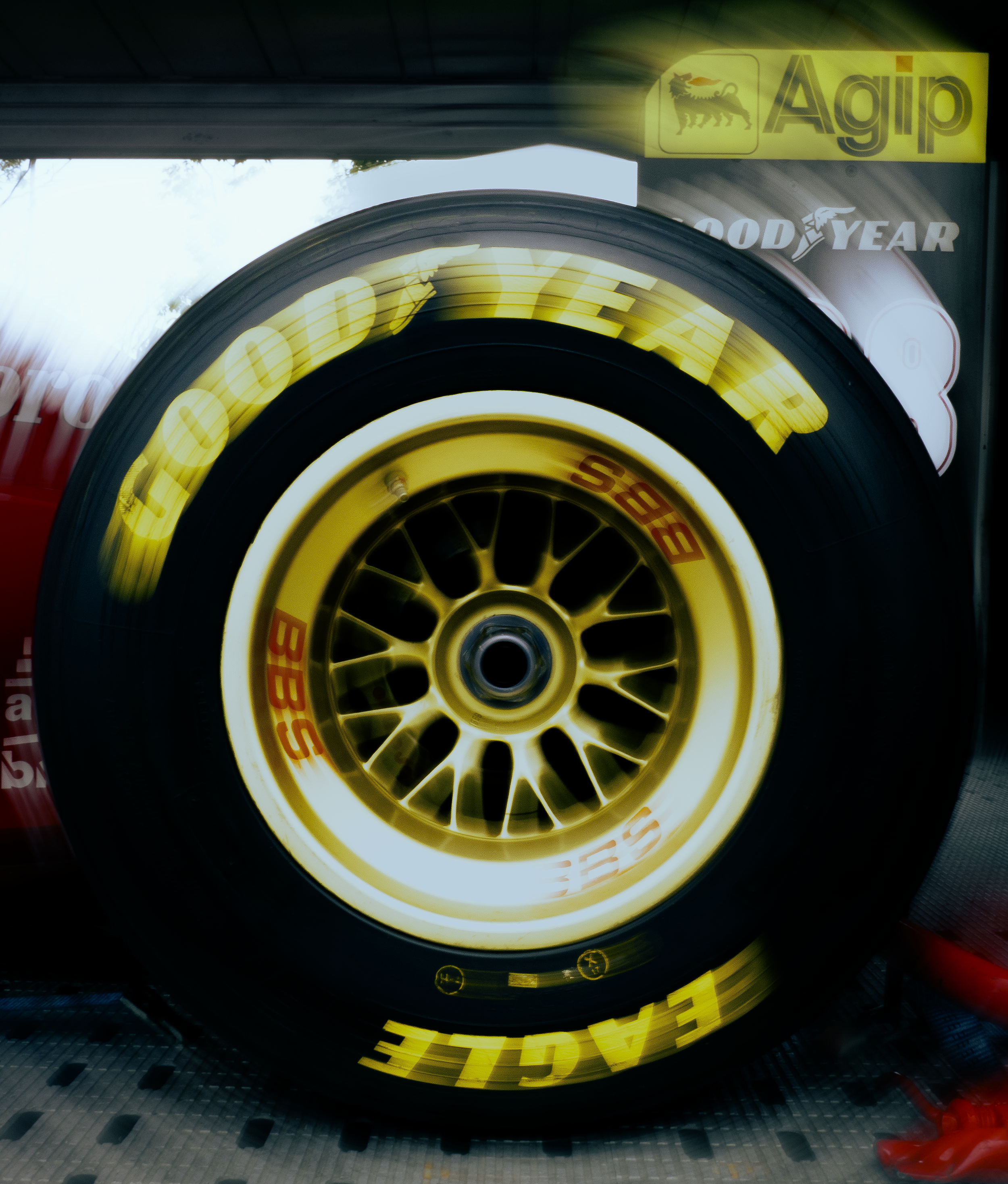 Une roue de voiture de course avec des inscriptions en jaune et rouge, et des logos de sponsors, dans un stand ou une zone de garage.