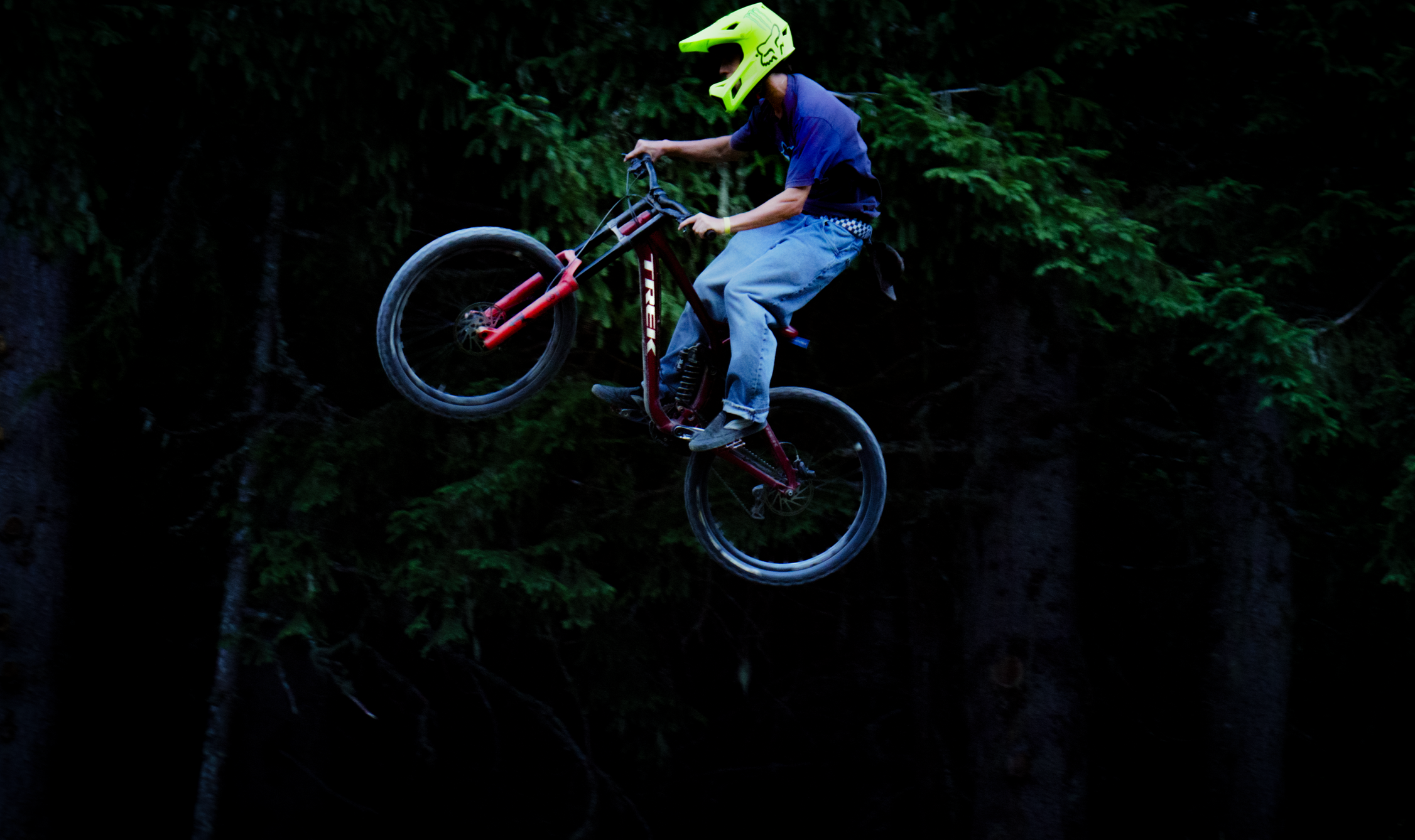 Personne en équipement de sécurité effectuant un saut en VTT dans une forêt