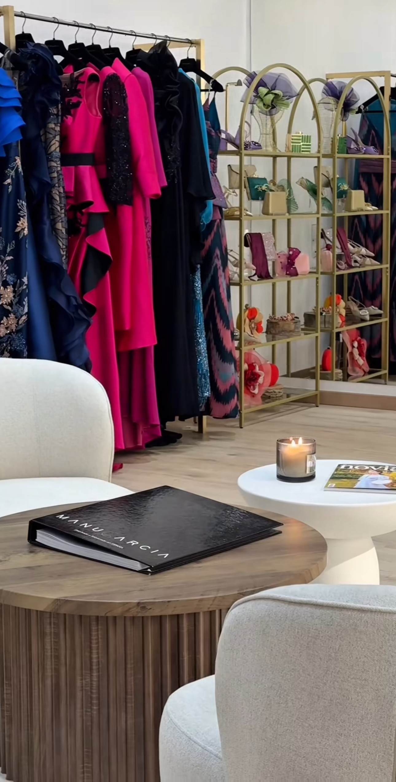 Ropa elegante en perchas y accesorios en estantes en un probador de vestir, con mesas y sillas blancas en primer plano.