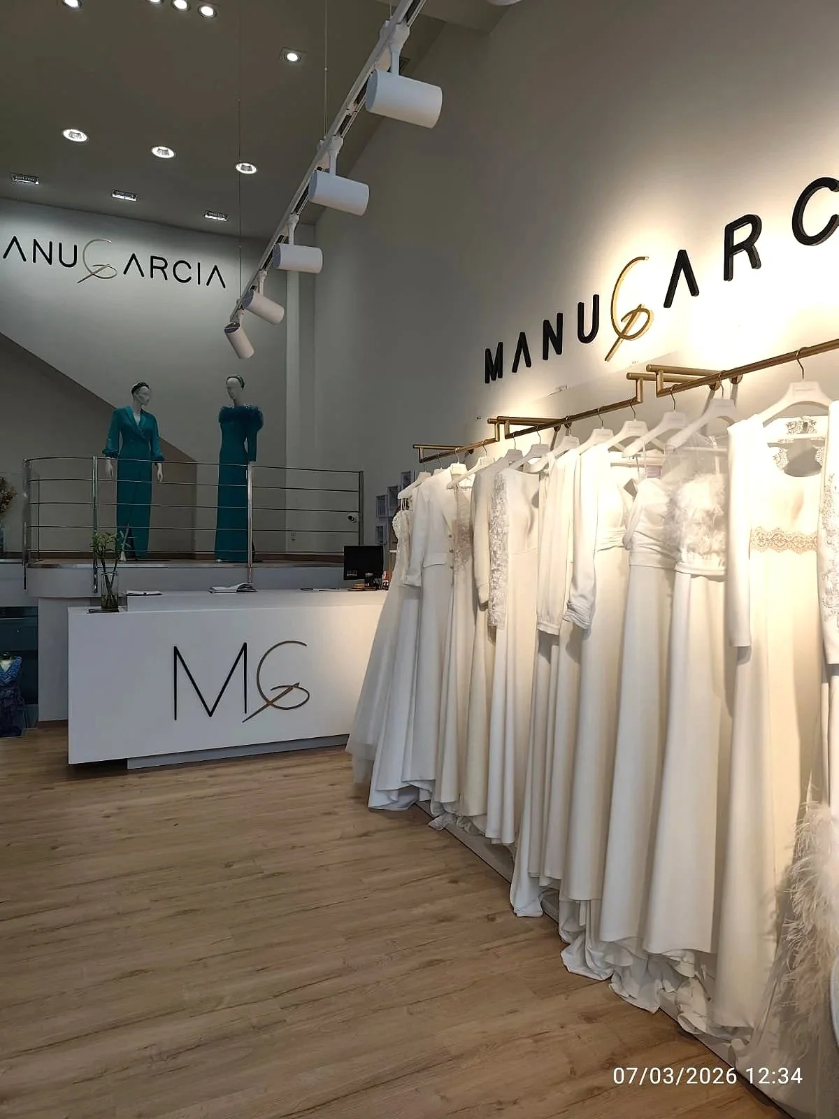 Vestido de novia blanco en exhibición con la marca Manuel García en la pared.