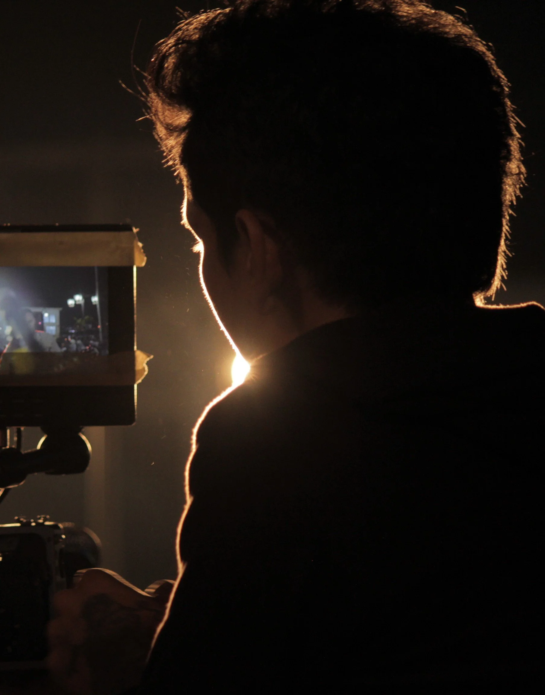 Silhouette of a man operating a camera or filming equipment with a bright light behind him.