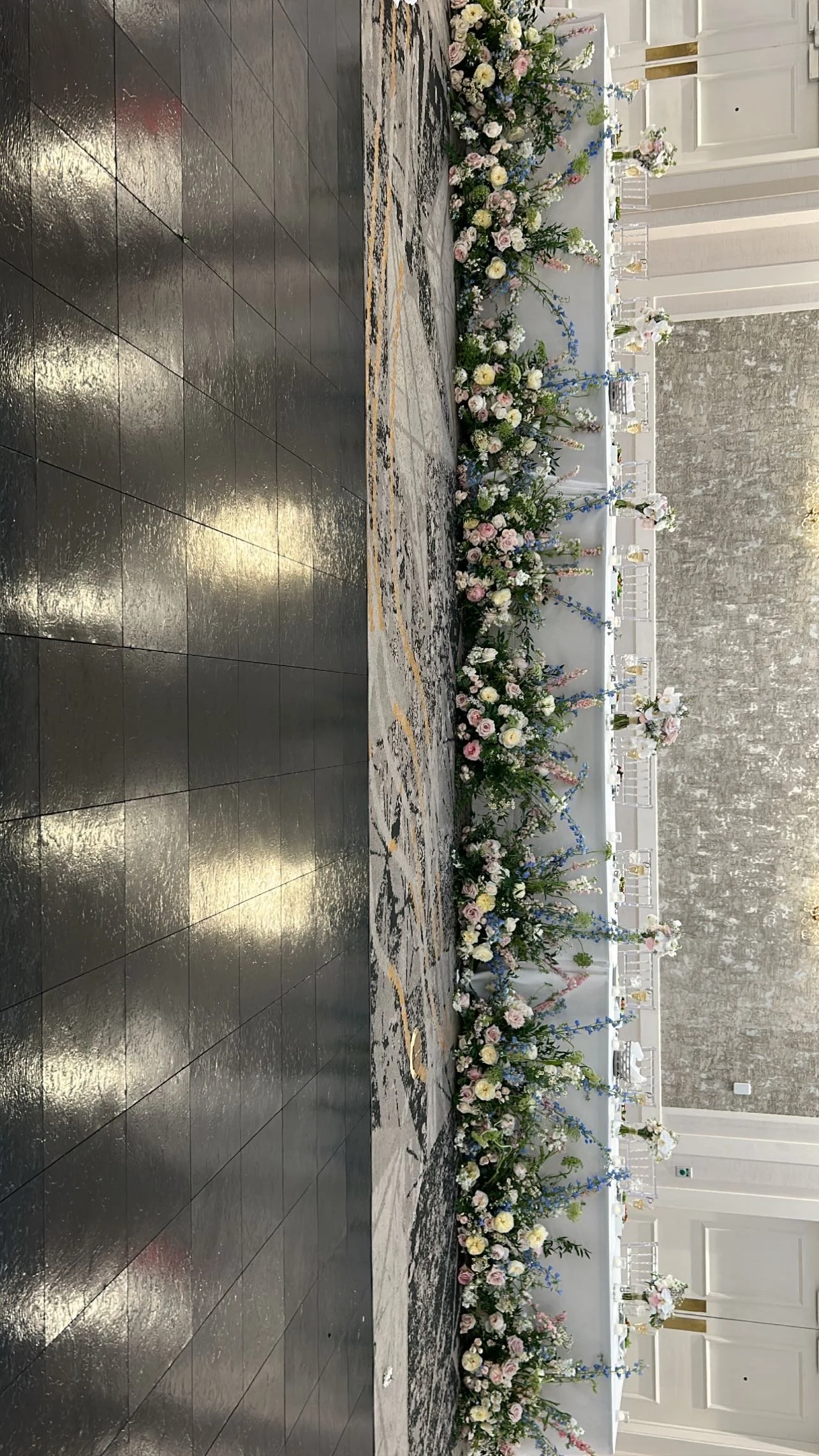 A beautifully decorated banquet table with floral arrangements on a long table, set for an event or celebration, with a patterned carpet and modern wall decor in the background.
