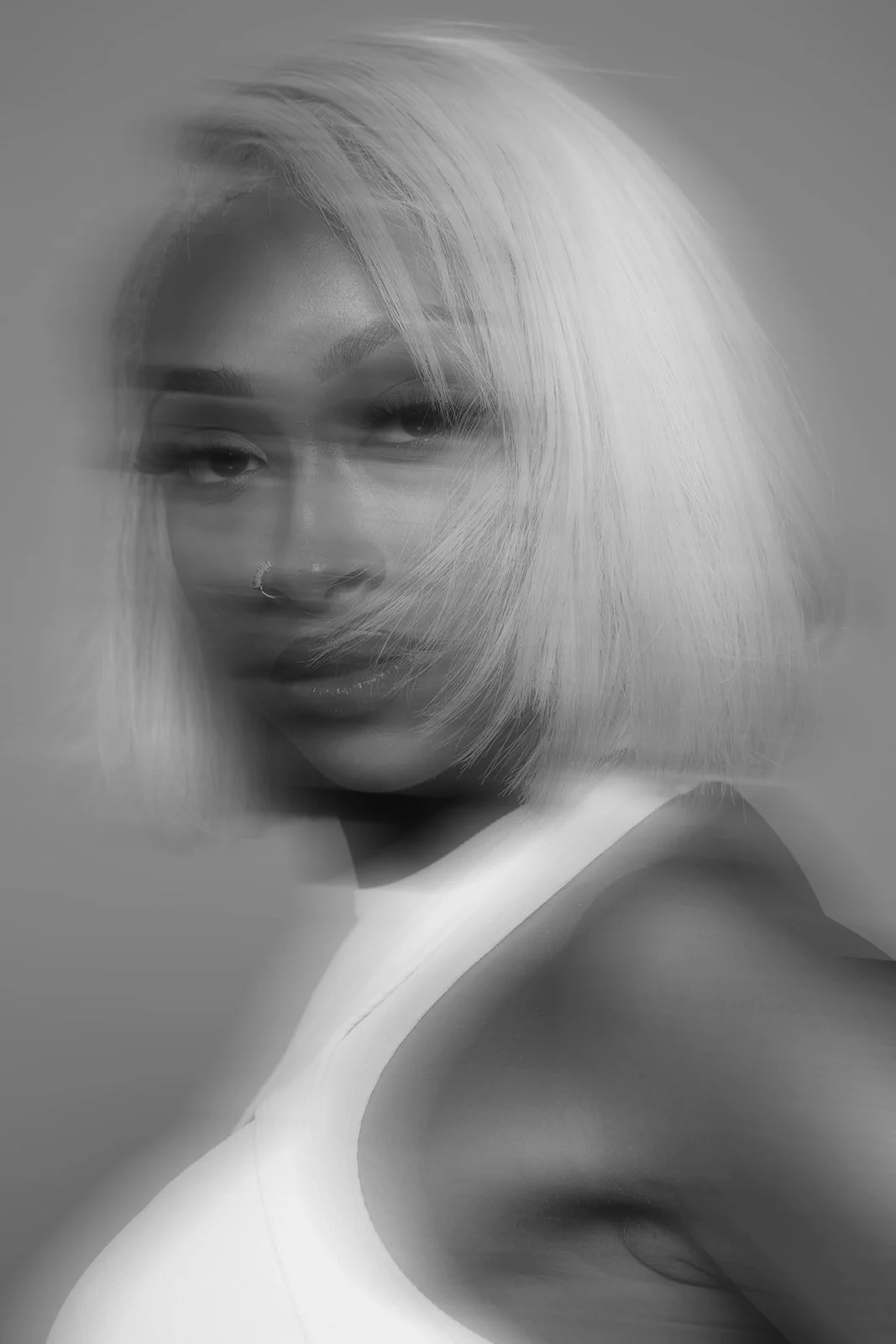 Black and white portrait of a woman with platinum blonde hair, wearing a white top, looking directly at the camera.