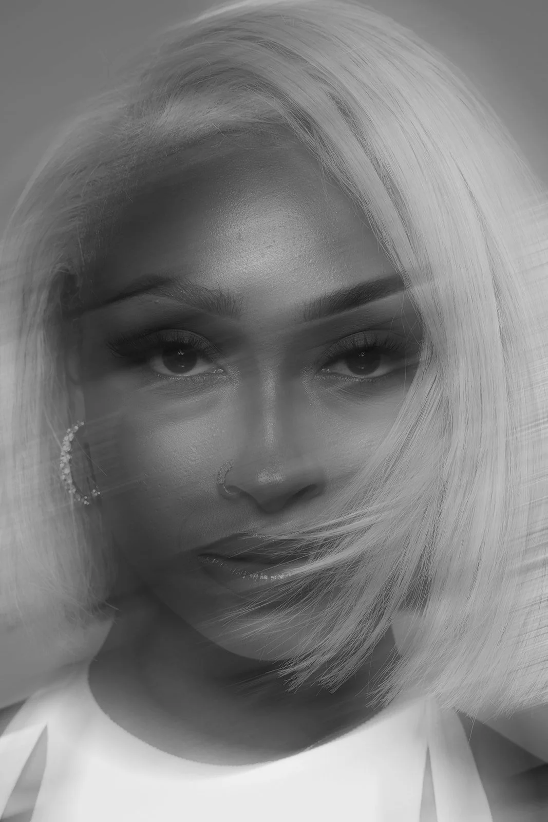 Close-up black and white portrait of a woman with platinum blonde hair, dark eyebrows, and earrings.