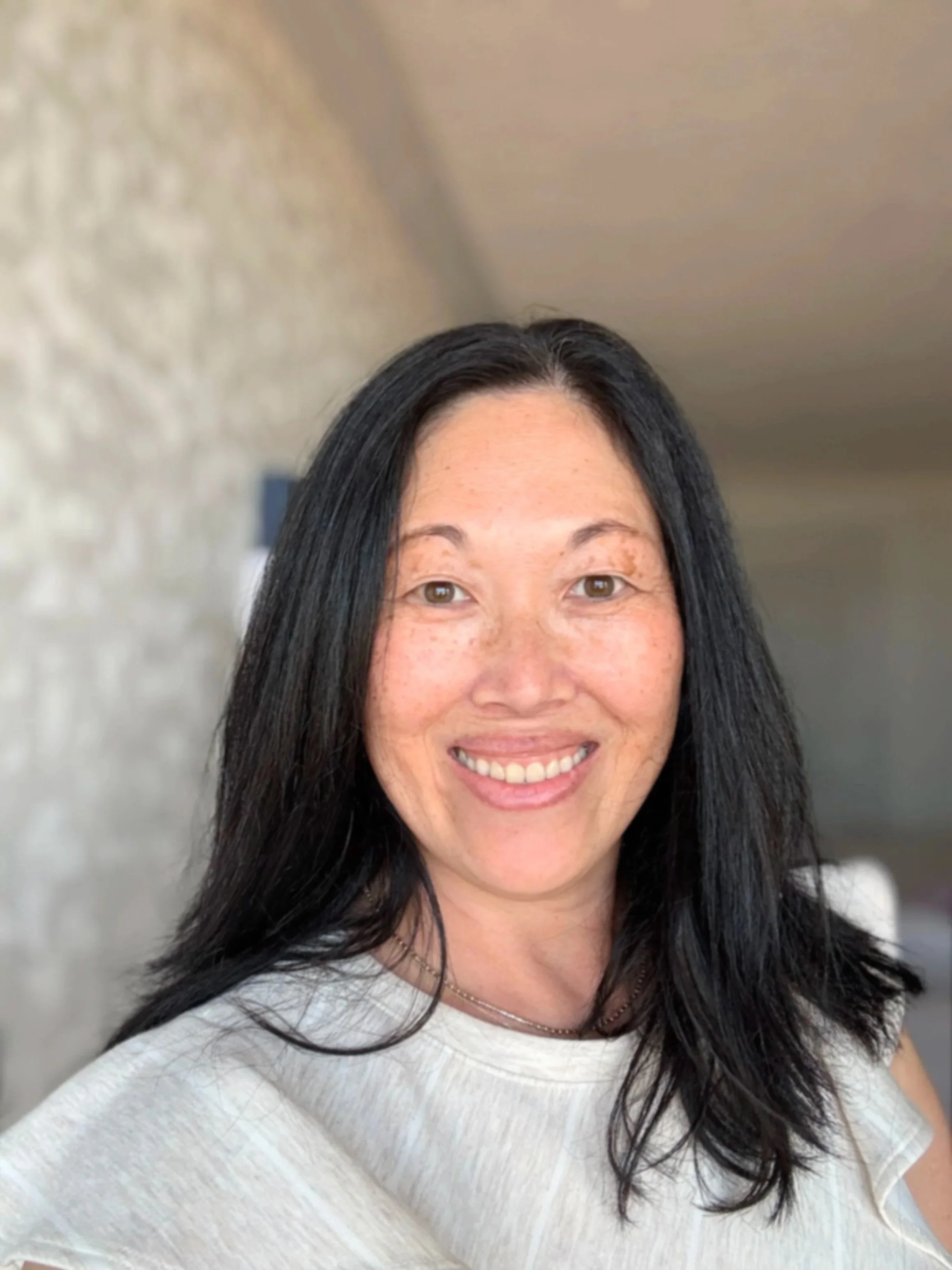A smiling woman with long black hair, wearing a light-colored top, introducing herself