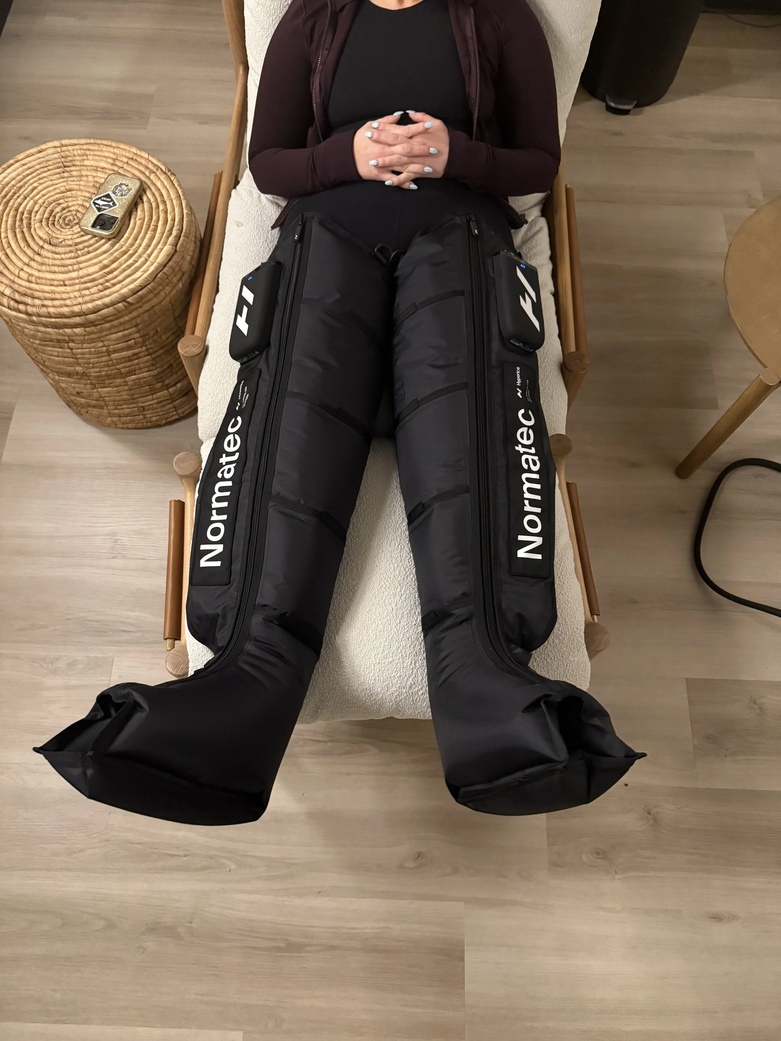 A person lying on a bed with their legs elevated, wearing black hockey pants with the brand name 'Normatec' printed on the sides.