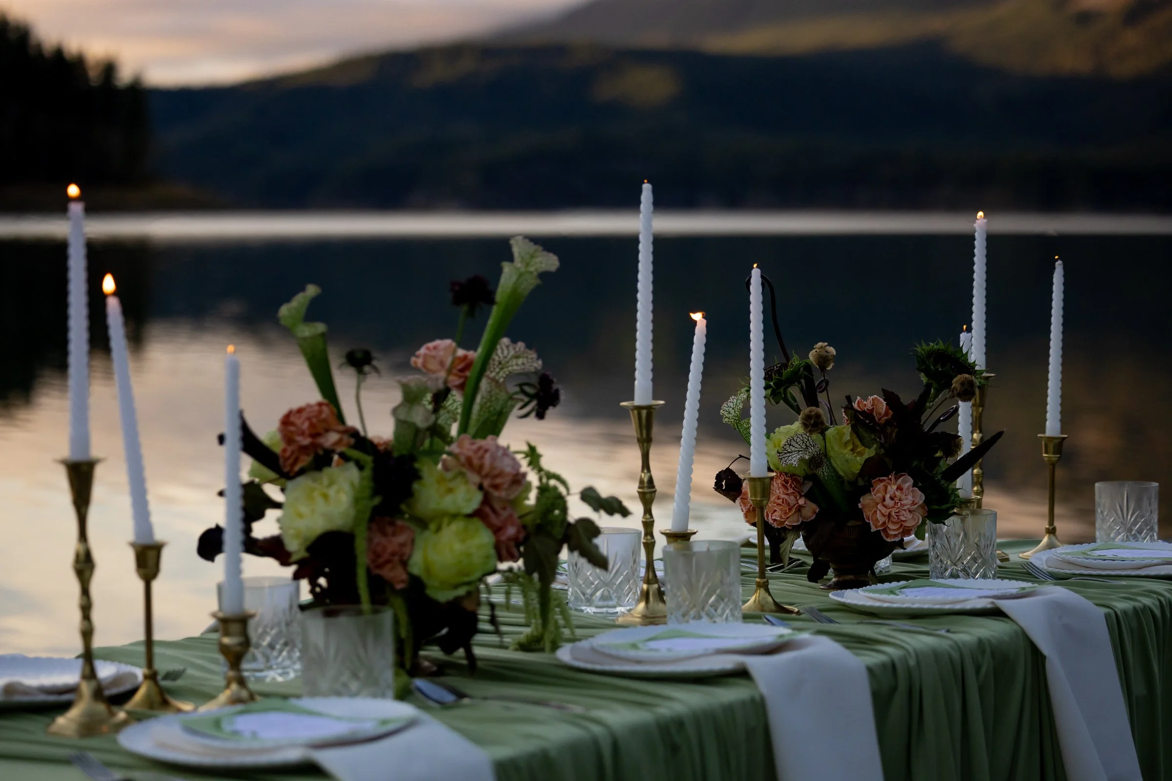 tablescape on waterfront with candles, a mountain backdrop, whimsical centerpieces, with pink green and brown flowers