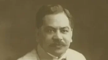 Black-and-white photo of a man with a mustache wearing a suit and tie, smiling slightly.