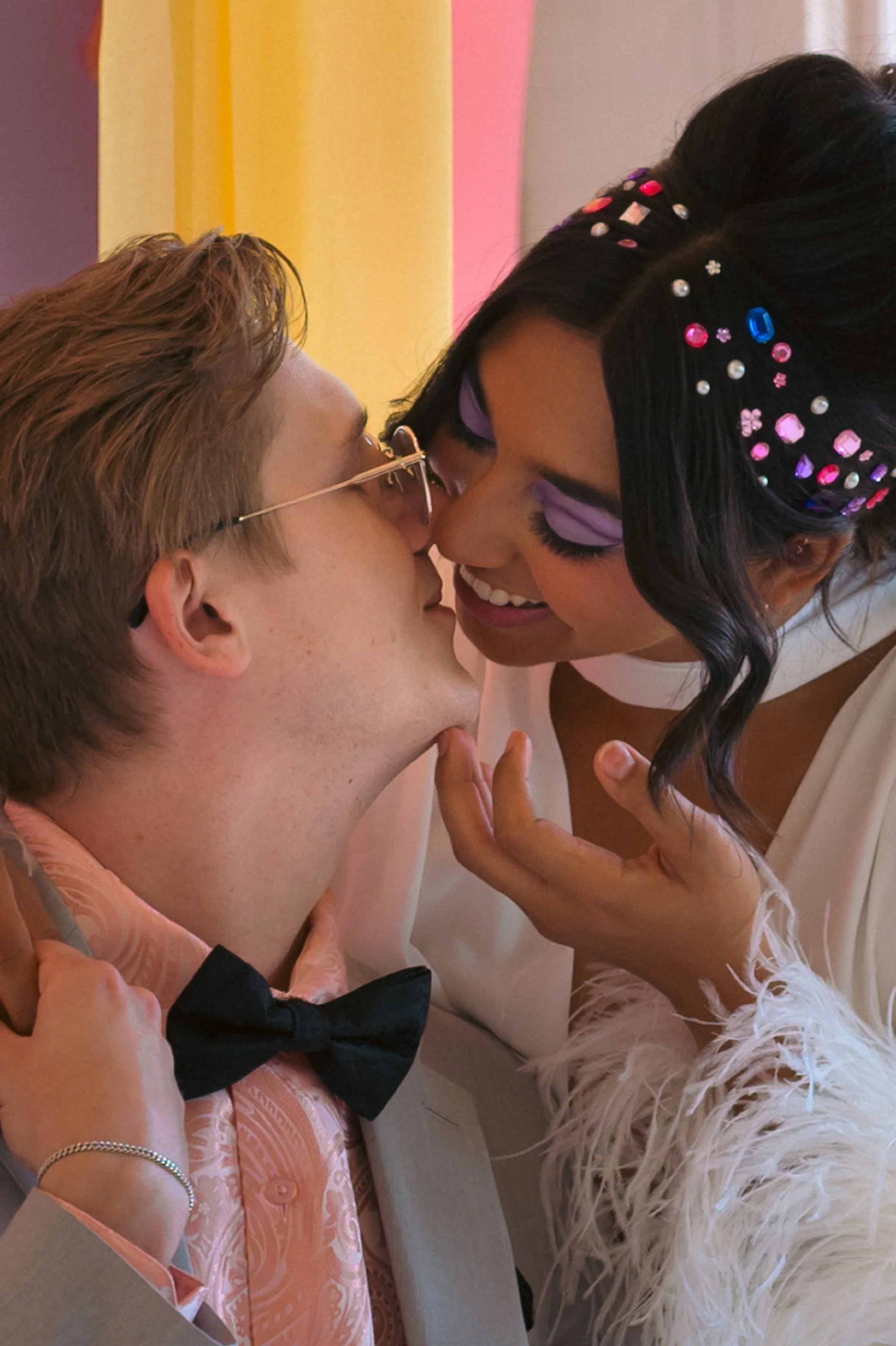 A romantic moment between a man with glasses and a woman with a colorful hair accessory, close together and about to kiss.