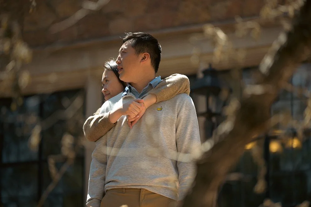 A boy receiving a hug from a girl outdoors in front of a house with trees and warm lighting.