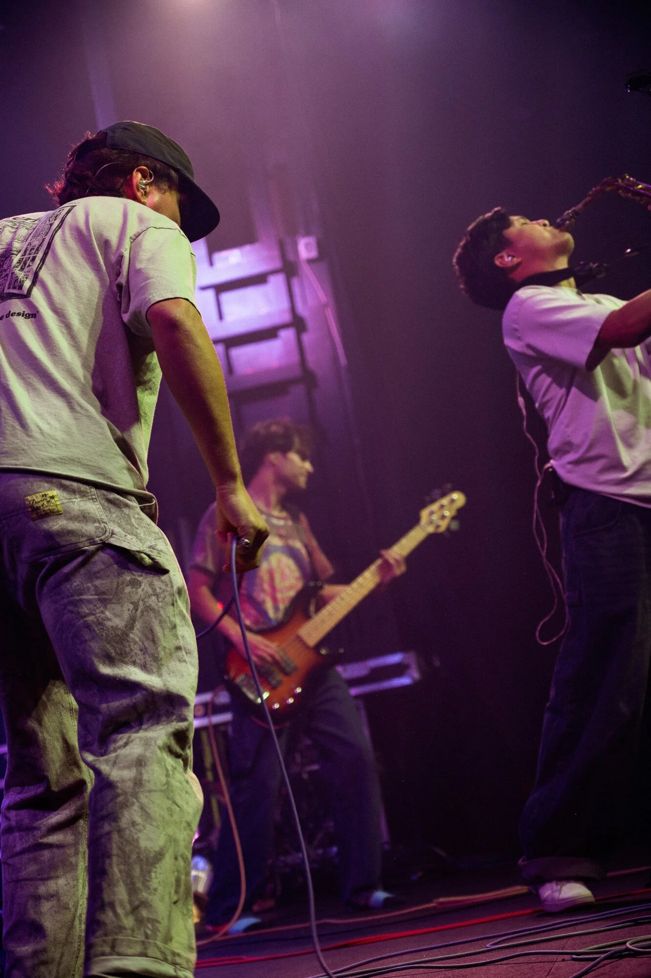 A band performing on stage with a singer, guitarist, and saxophonist in a dimly lit setting with purple lighting.