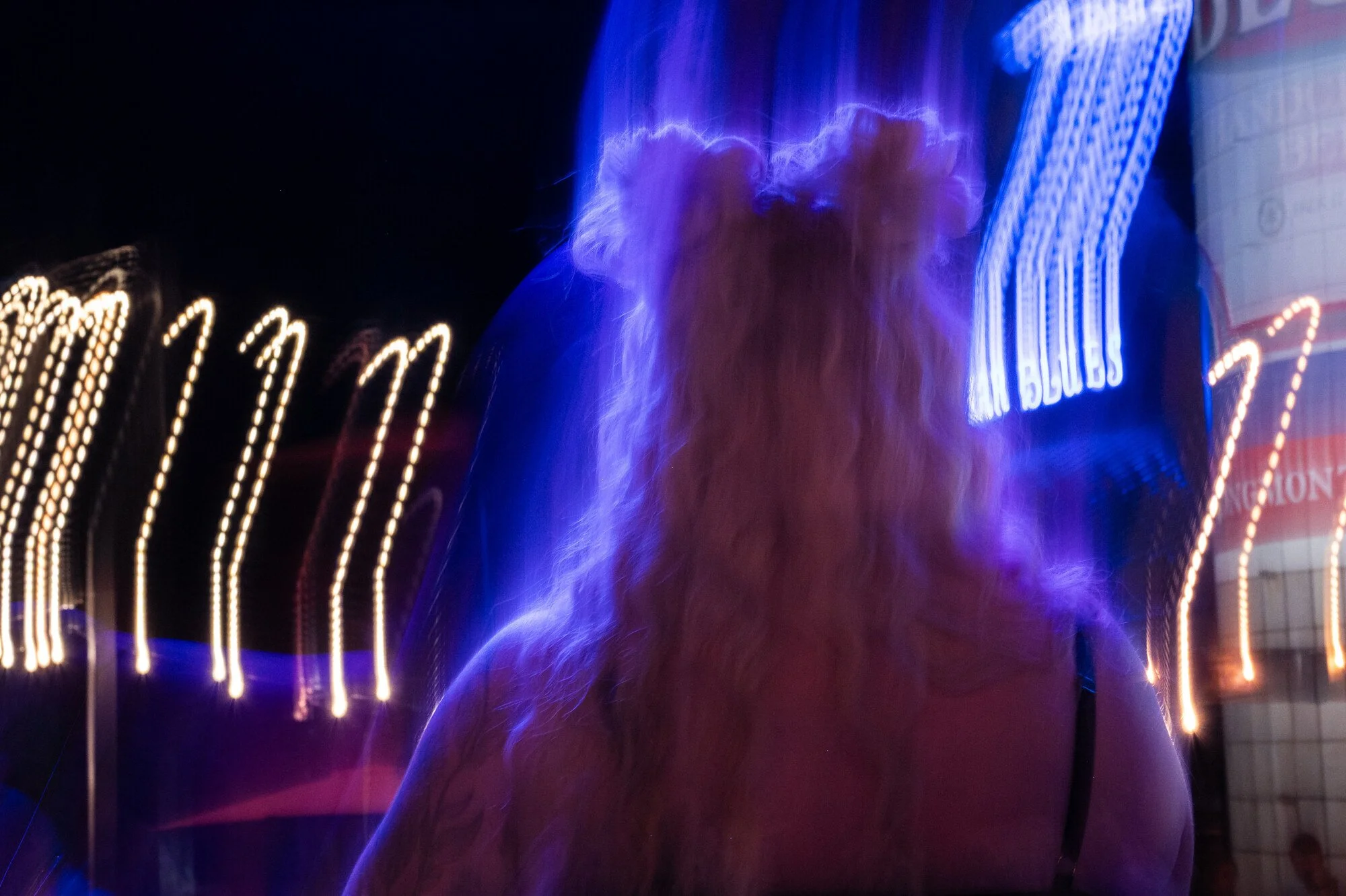 A dog with light brown fur standing in front of bright blue neon lights at night, creating a glowing effect around the dog.