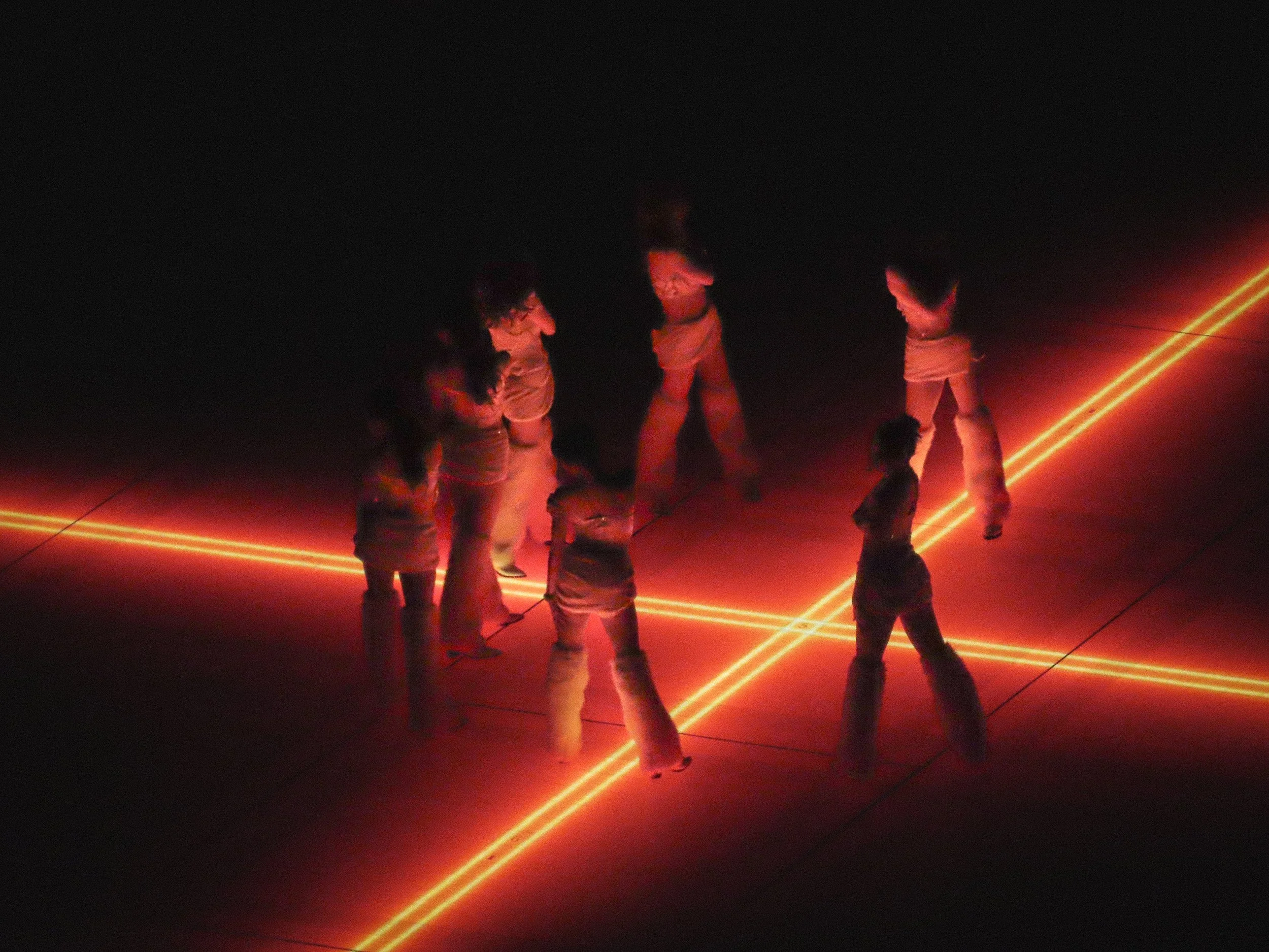 Group of six people standing in a dark room illuminated by red laser lights forming horizontal and diagonal lines on the floor and walls.