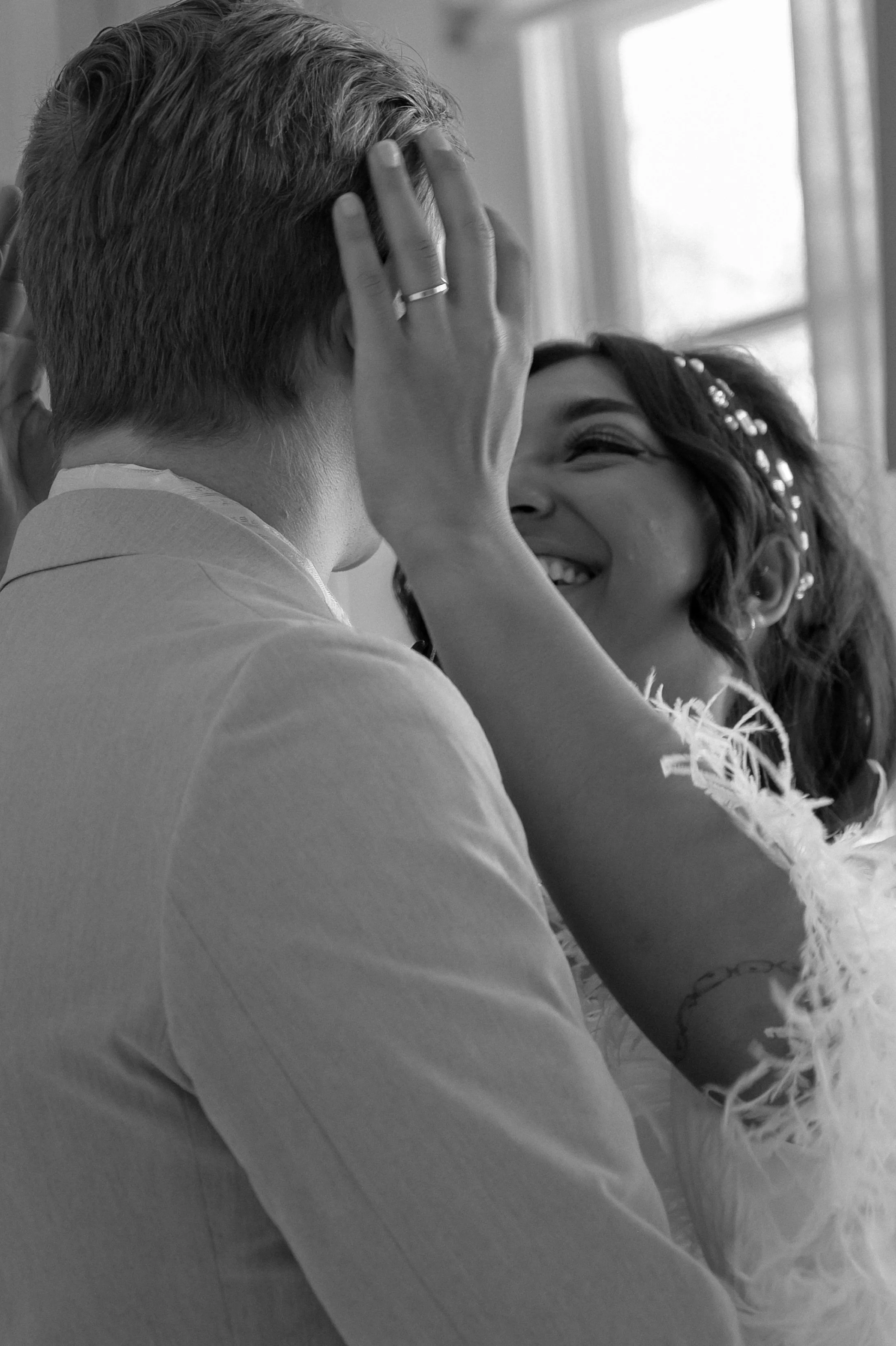 A woman with earrings smiling while a man with short hair and a ring on his finger touch each other's faces.