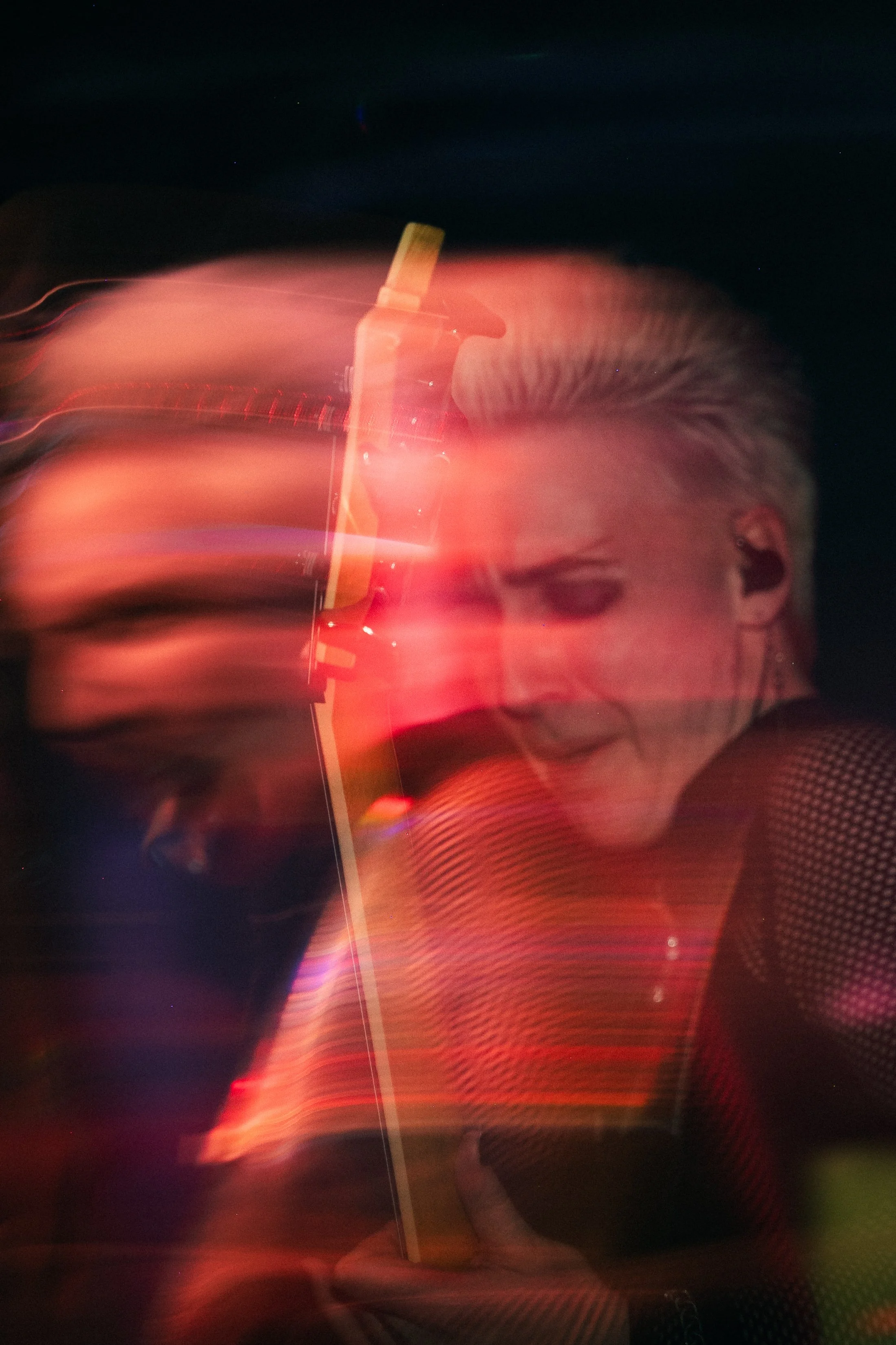 Blurred image of a person with blonde hair holding a drink with a straw, with rainbow-like light streaks across the image.