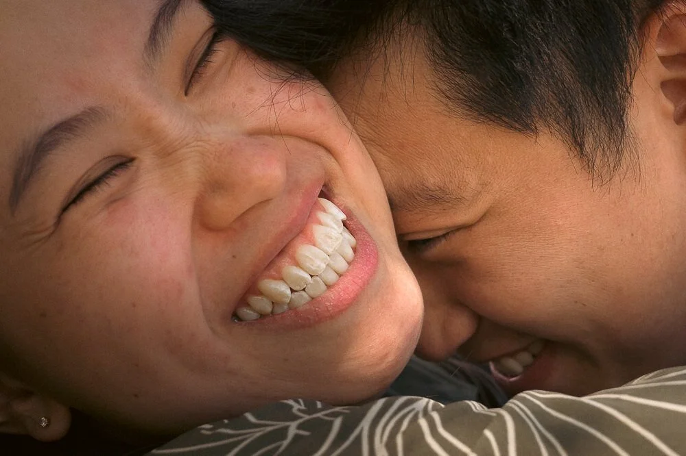 A close-up of a man and a woman smiling and laughing together with their faces close, showing joy and affection.