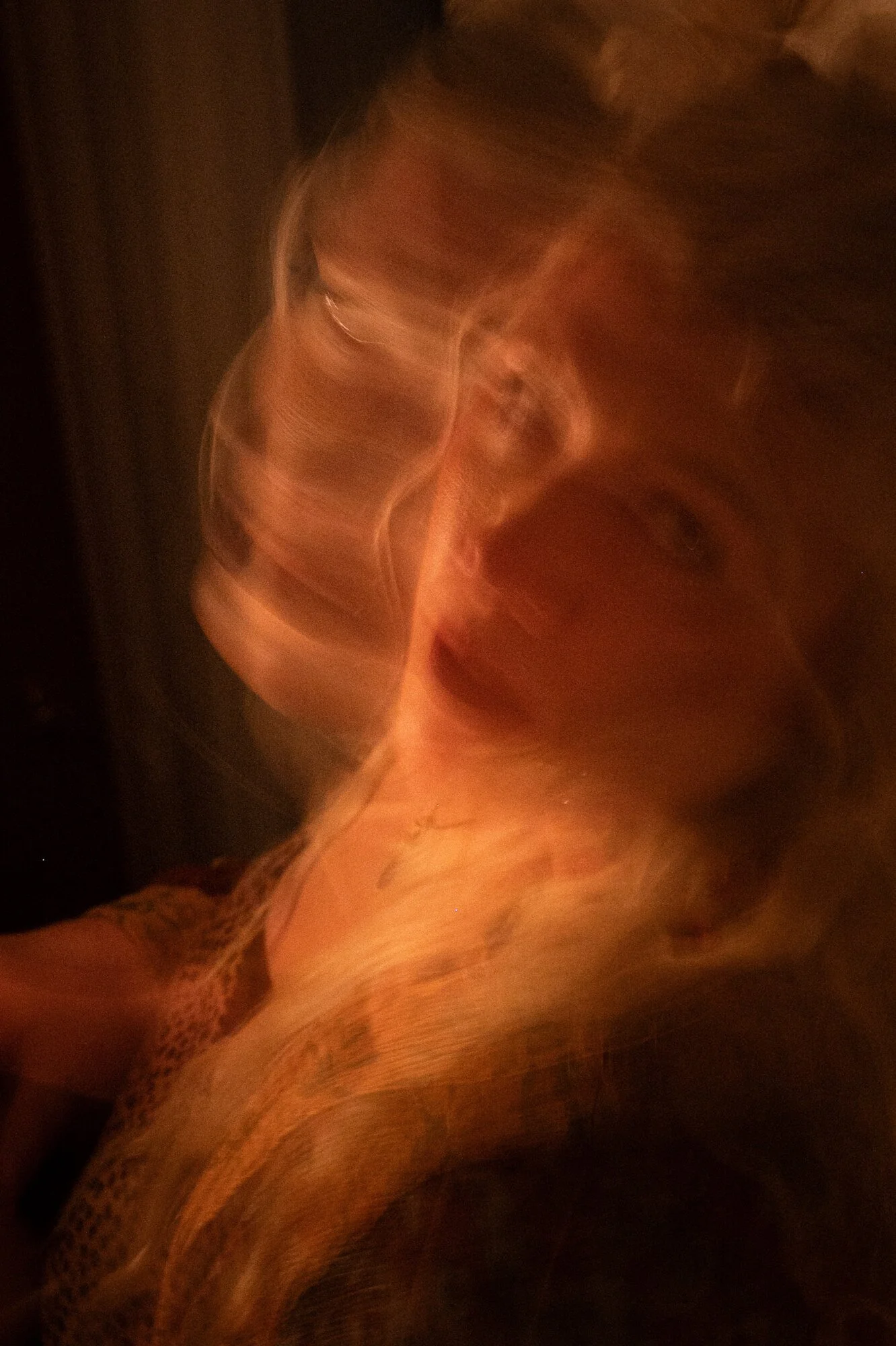 A person with long hair, tattoos on the shoulder and arm, wearing a leopard print top, in a low-light setting.