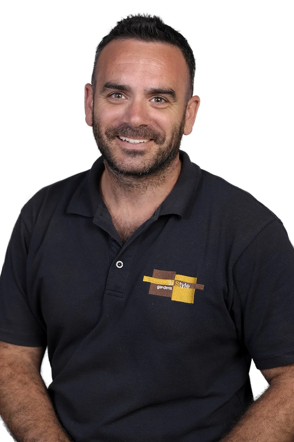 A man with dark hair and a beard smiling, wearing a black polo shirt with a logo on the chest that has the words 'garden style'.