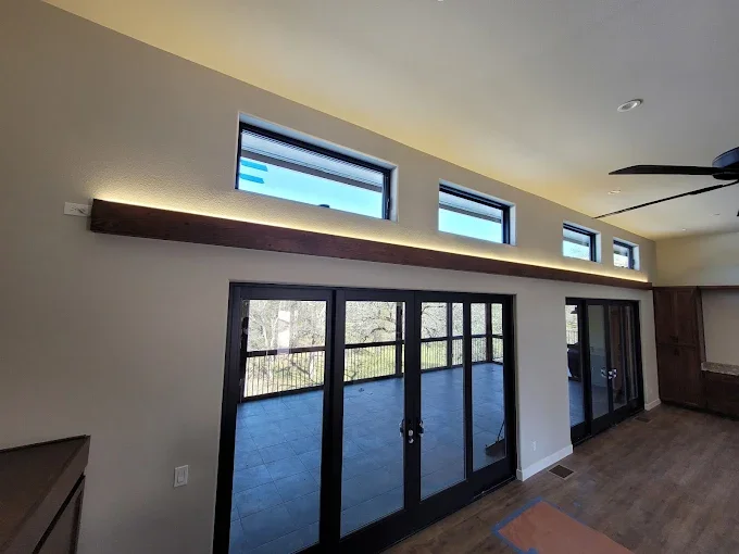 Modern living room with large sliding glass doors leading to a balcony, high rectangular windows above, dark wood trim, and a ceiling fan.