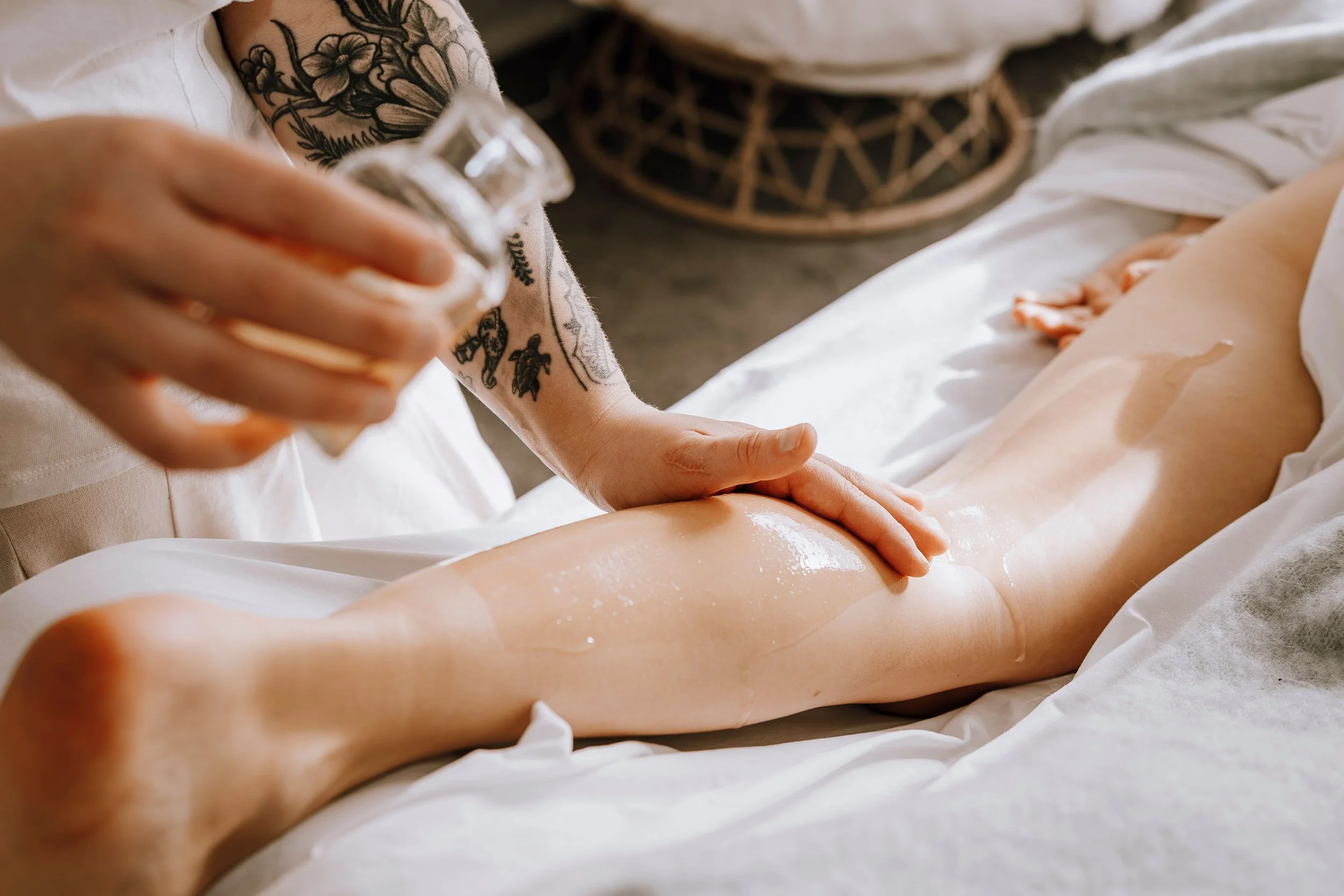 A person with tattoos is applying lotion or oil to a person's leg during a massage.