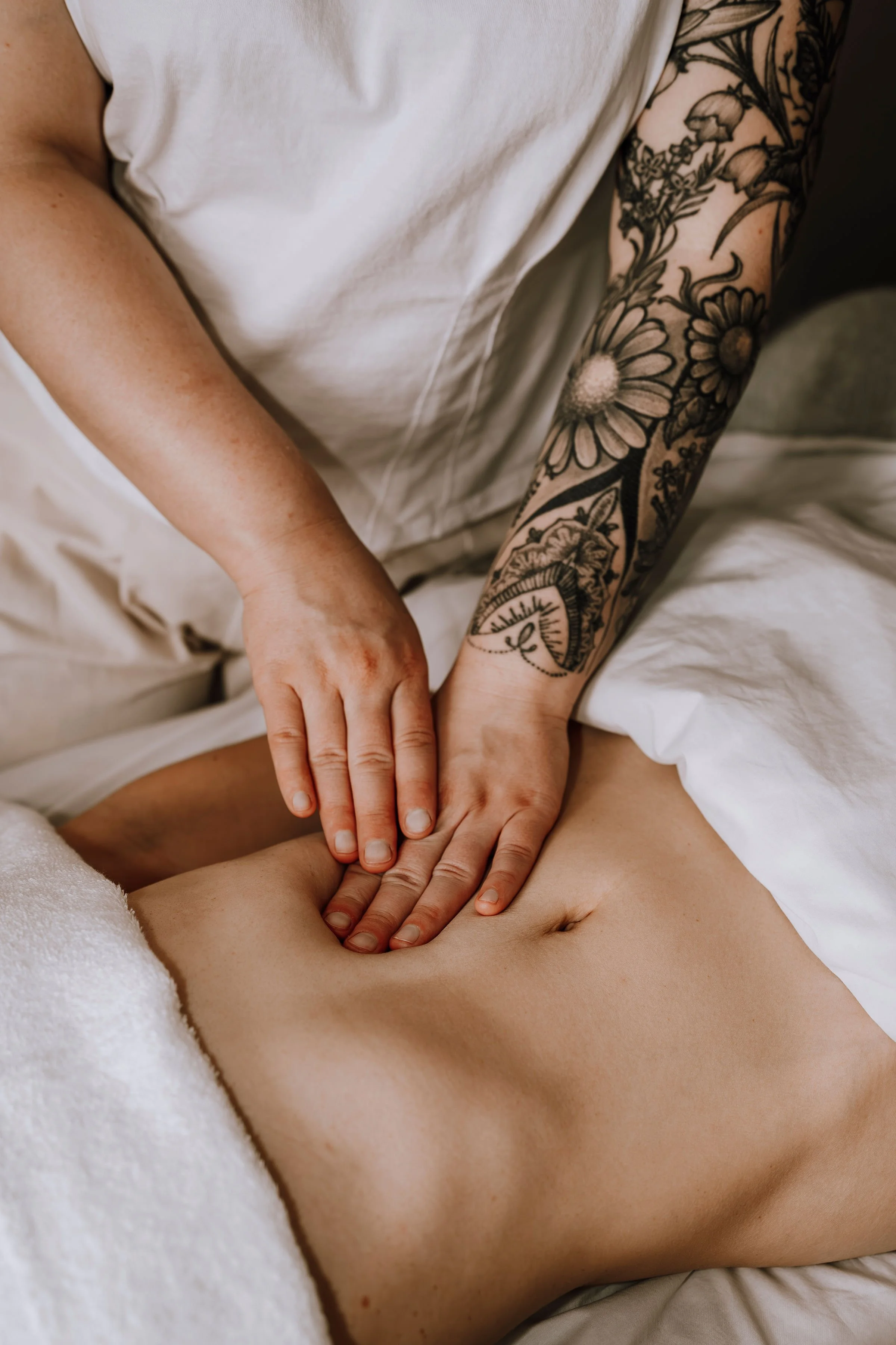 Person receiving a massage on their abdomen from a massage therapist with tattooed arms.