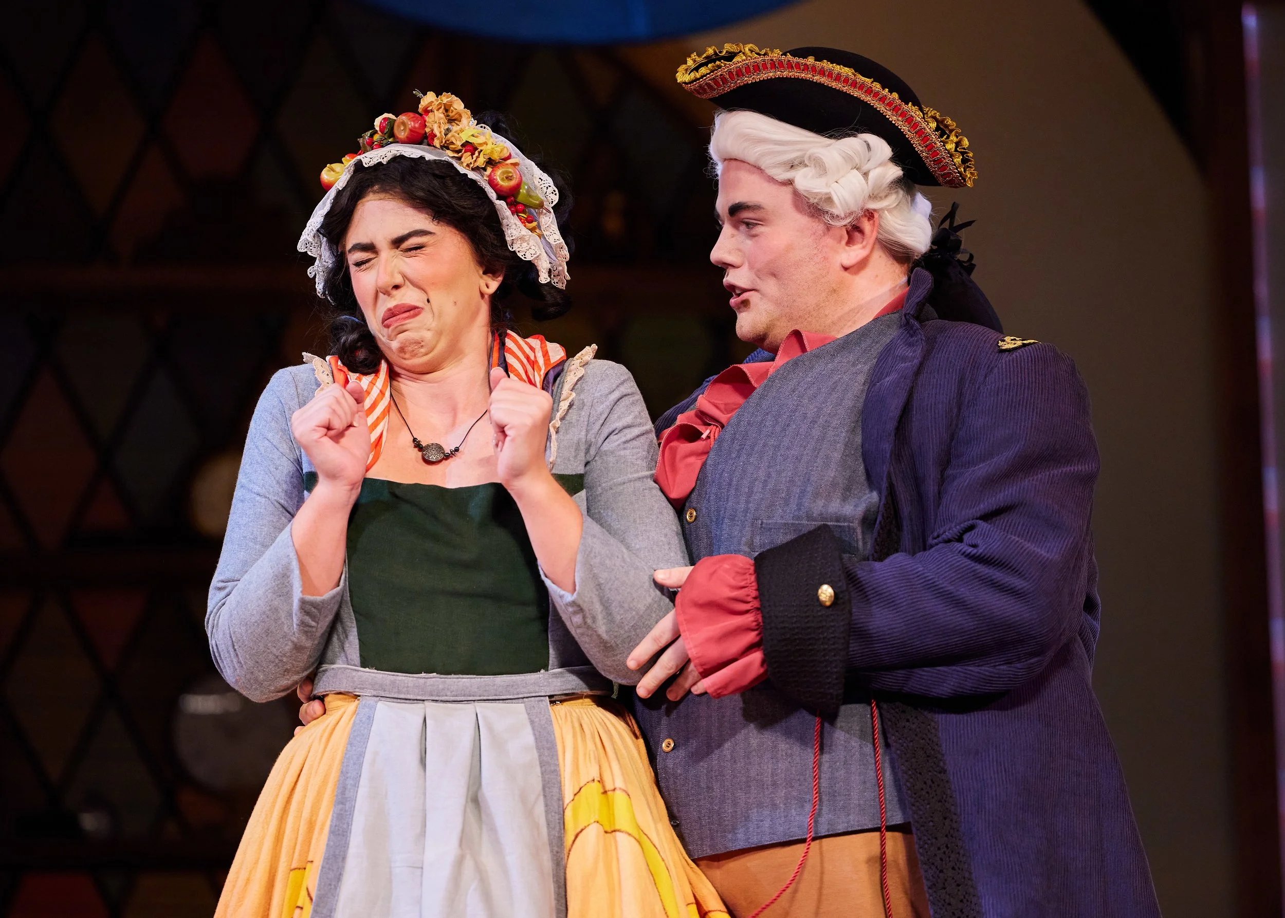 Two actors in period costumes performing on stage, with the woman appearing emotional and the man speaking.