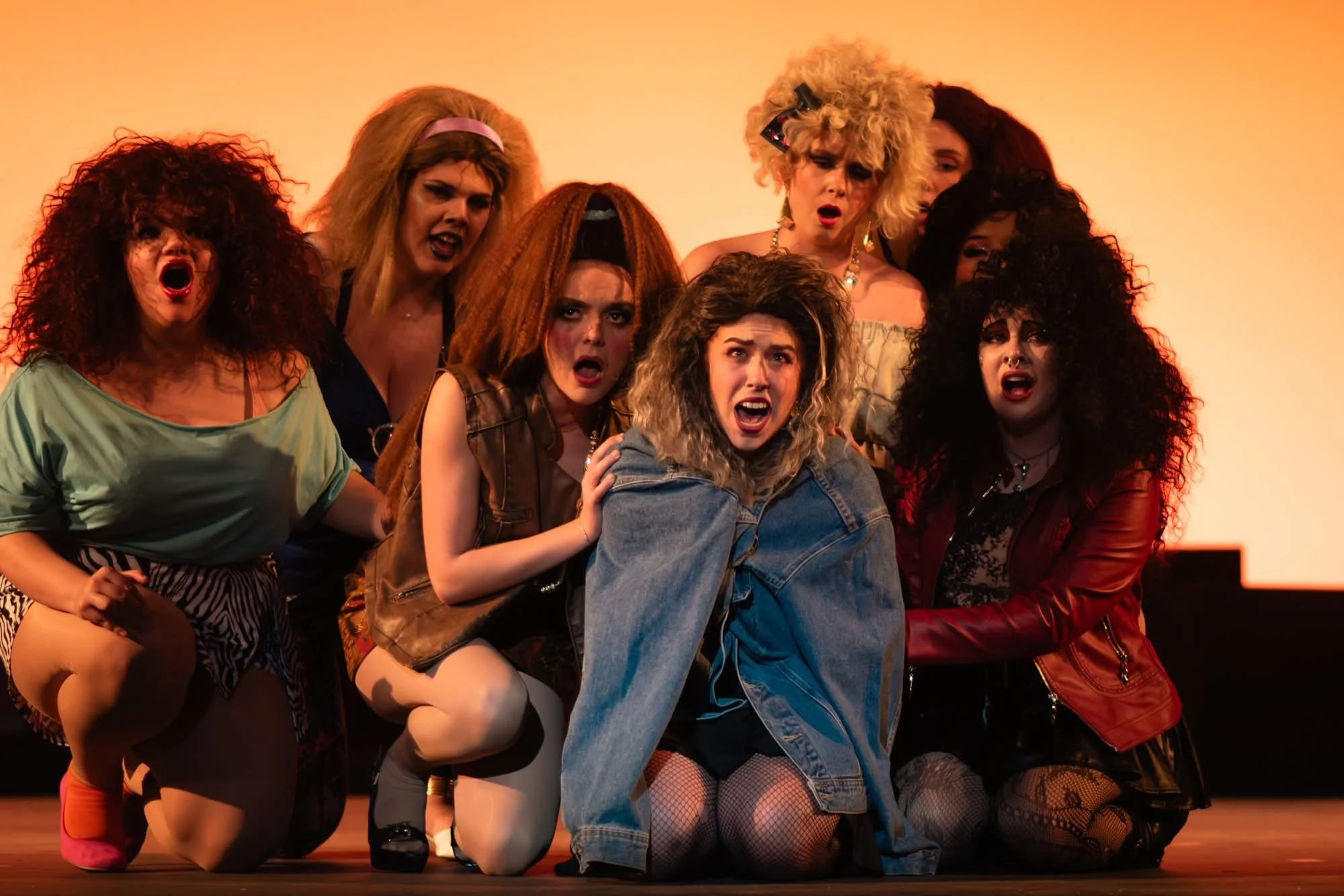 Group of women in colorful costumes and makeup, performing on stage with dramatic expressions.