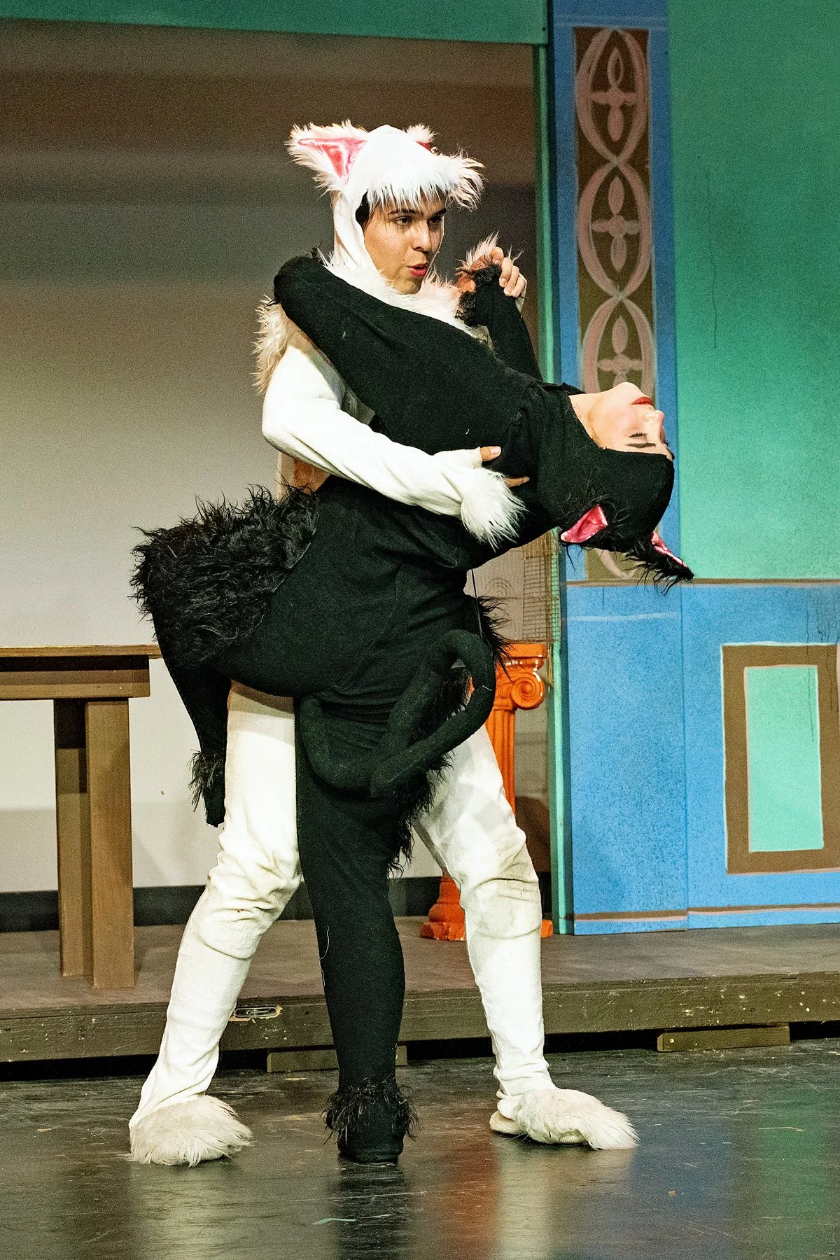 Two actors dressed in cat costumes performing on stage, with one actor holding the other in a dramatic pose during a theatrical play.