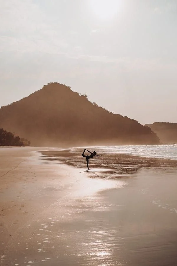 A person practicing yoga on a beach with a mountain in the background, during sunset or sunrise.