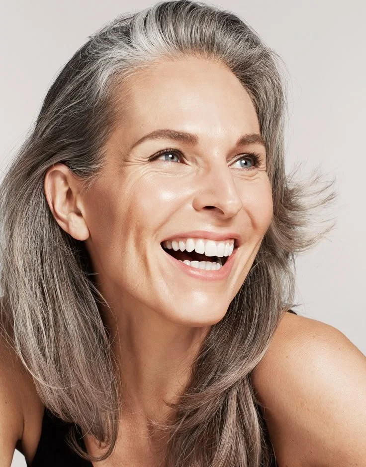 Close-up of a smiling middle-aged woman with gray hair and blue eyes, looking happy.