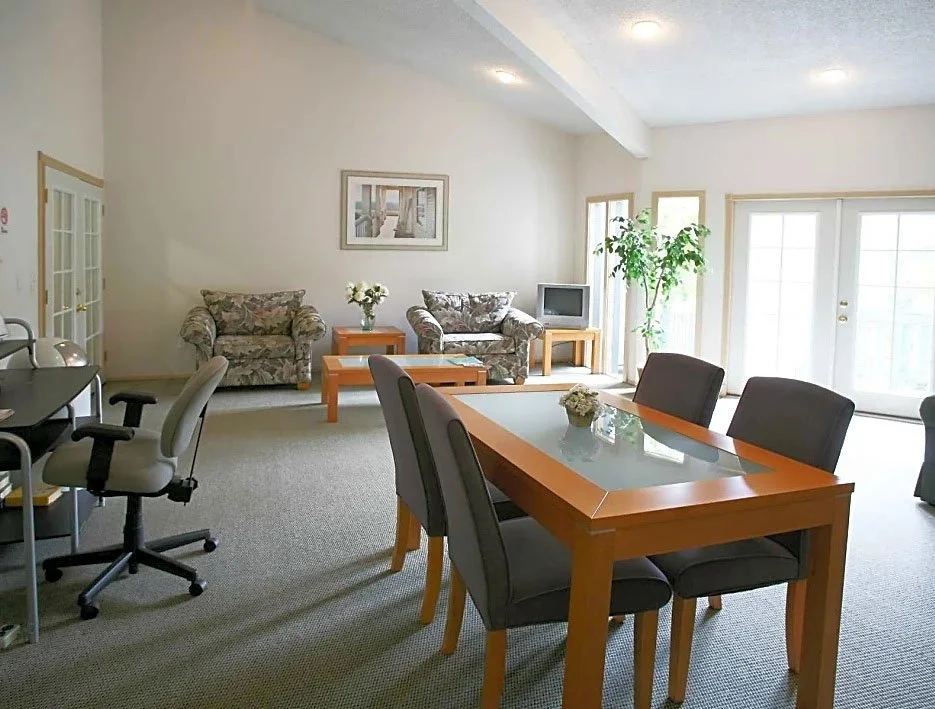 Living room and dining area with sofa, armchair, coffee tables, dining table with chairs, a TV, potted plant, and sliding glass doors.