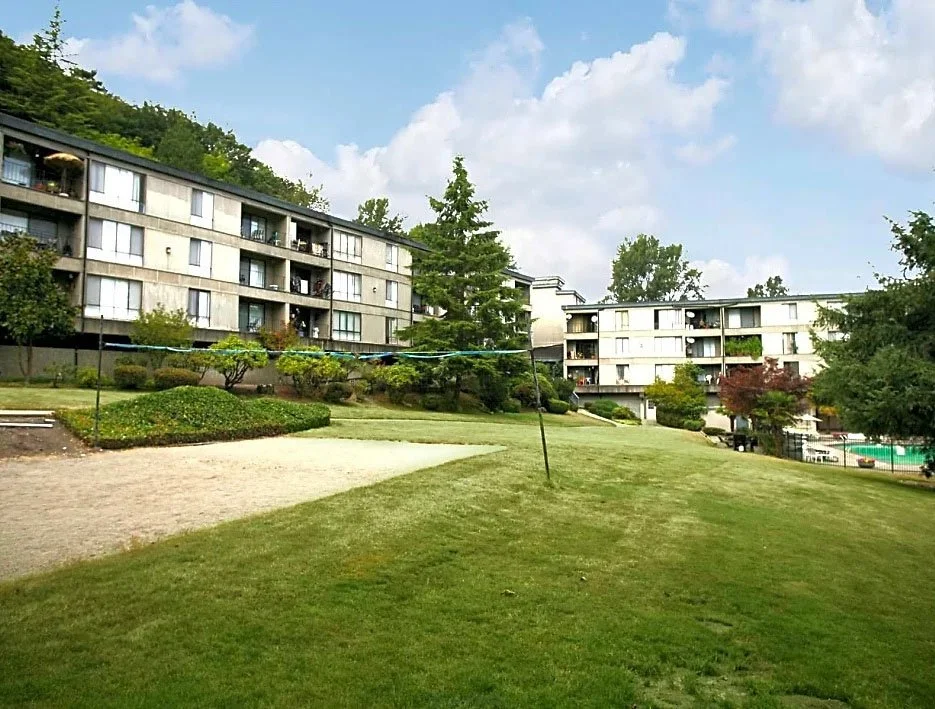 Apartment buildings with balconies overlooking a grassy courtyard with a clothesline and trees.