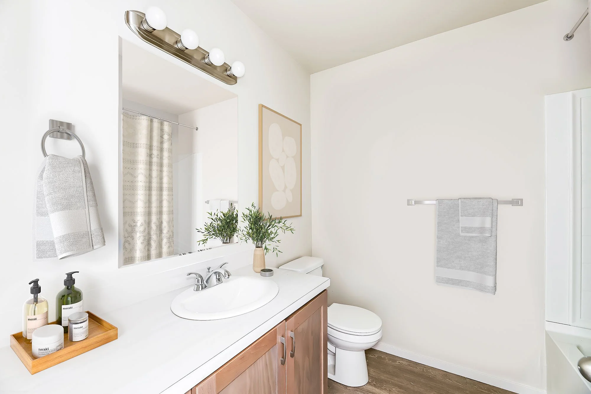 A bright bathroom with a large mirror, vanity with sink, potted plants, framed artwork, towel on the wall, and shower curtain.