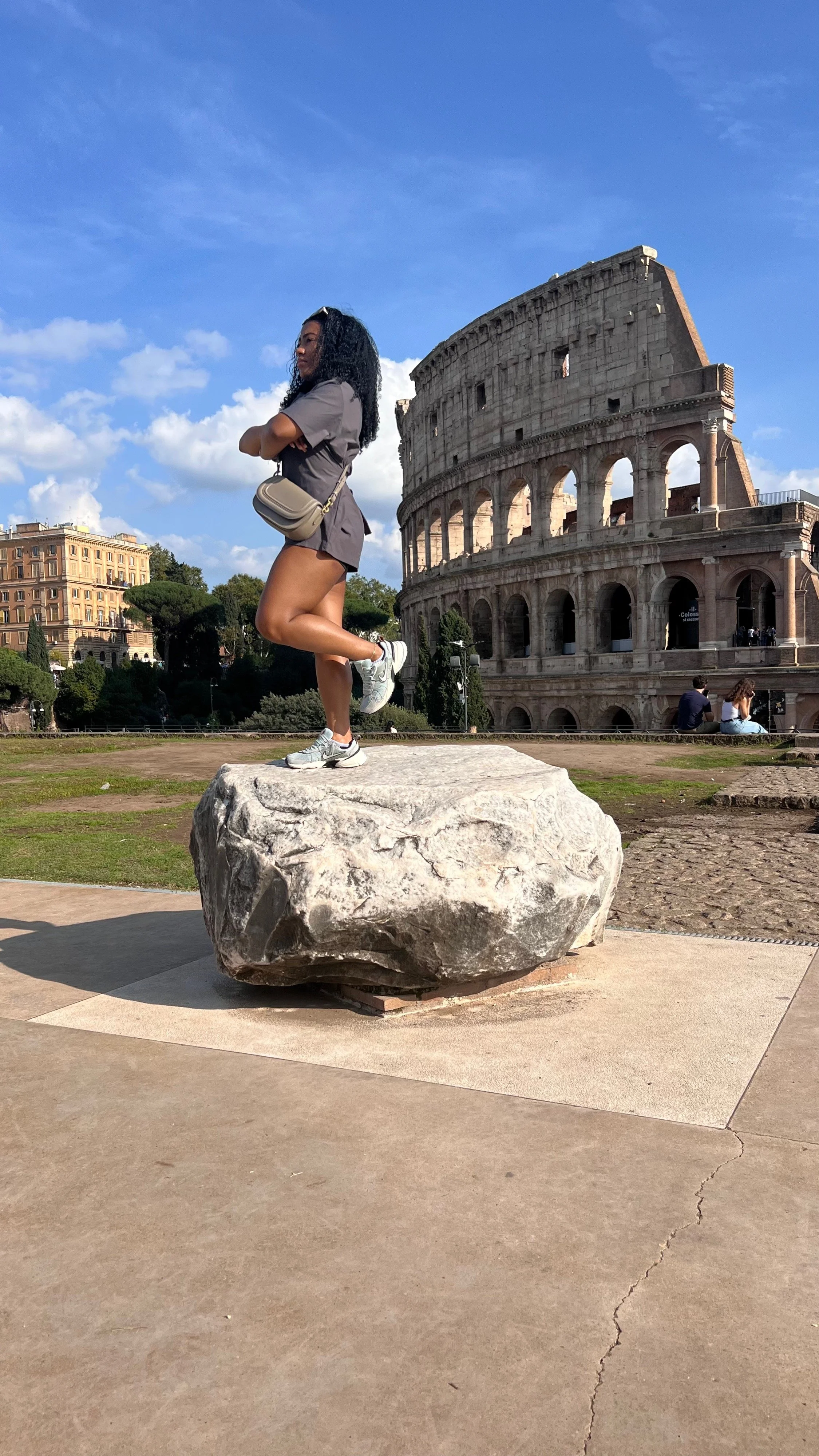 A woman standing on a large rock in front of the Colosseum in Rome