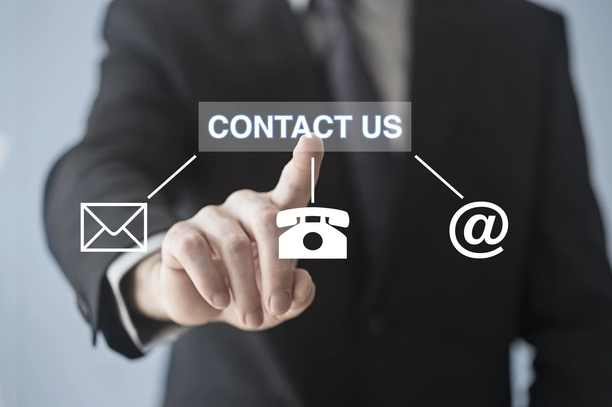 Business person in suit pointing at contact options, includes email icon, phone icon, and at symbol for email address.