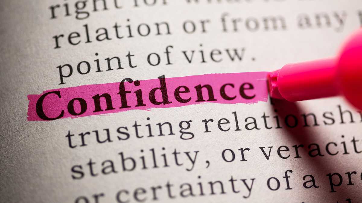A close-up of a page in a book with the word "confidence" highlighted in pink and a pink pen pointing to it.