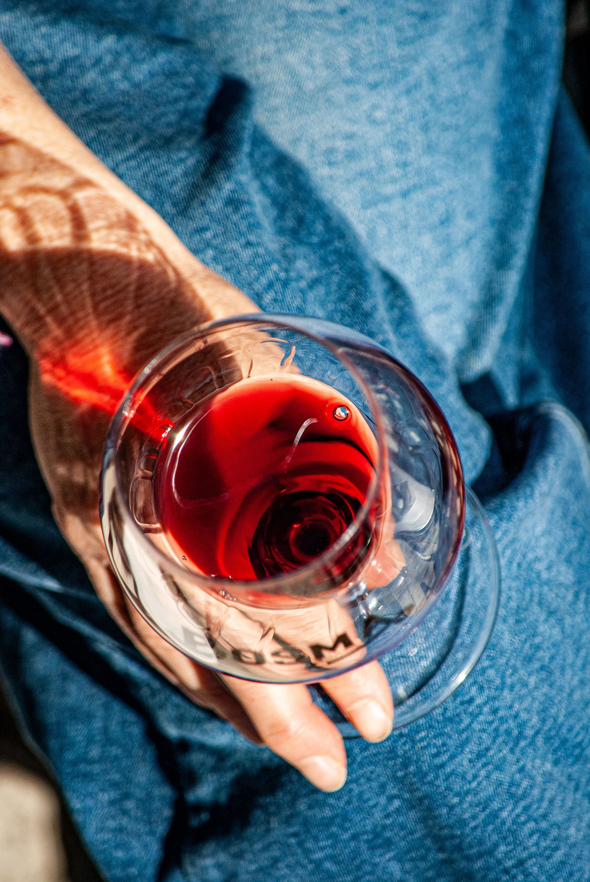 A person sitting on a lap, wearing blue jeans, holding a glass of red wine.