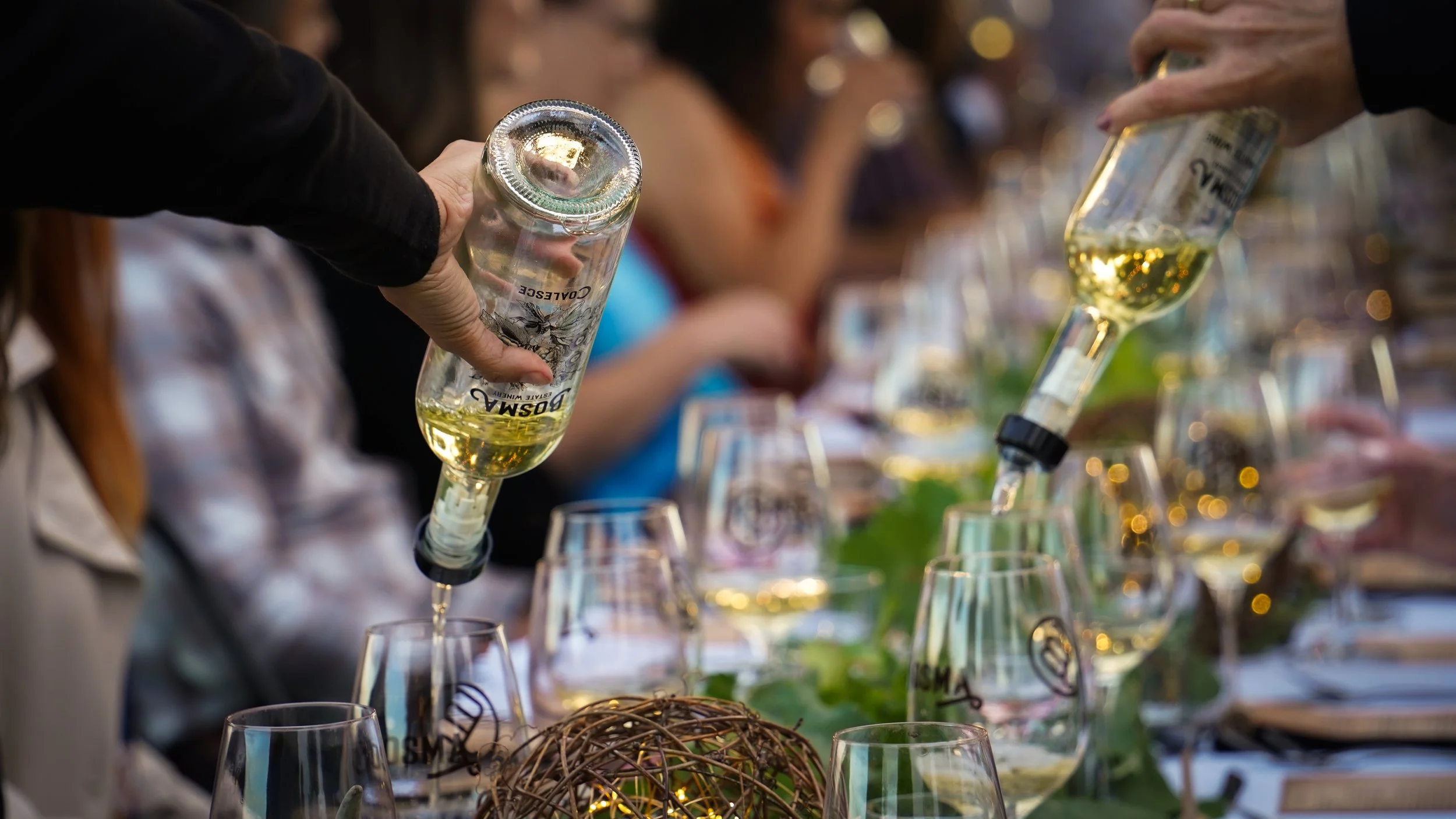 People pouring white wine into glasses at an outdoor event or celebration.