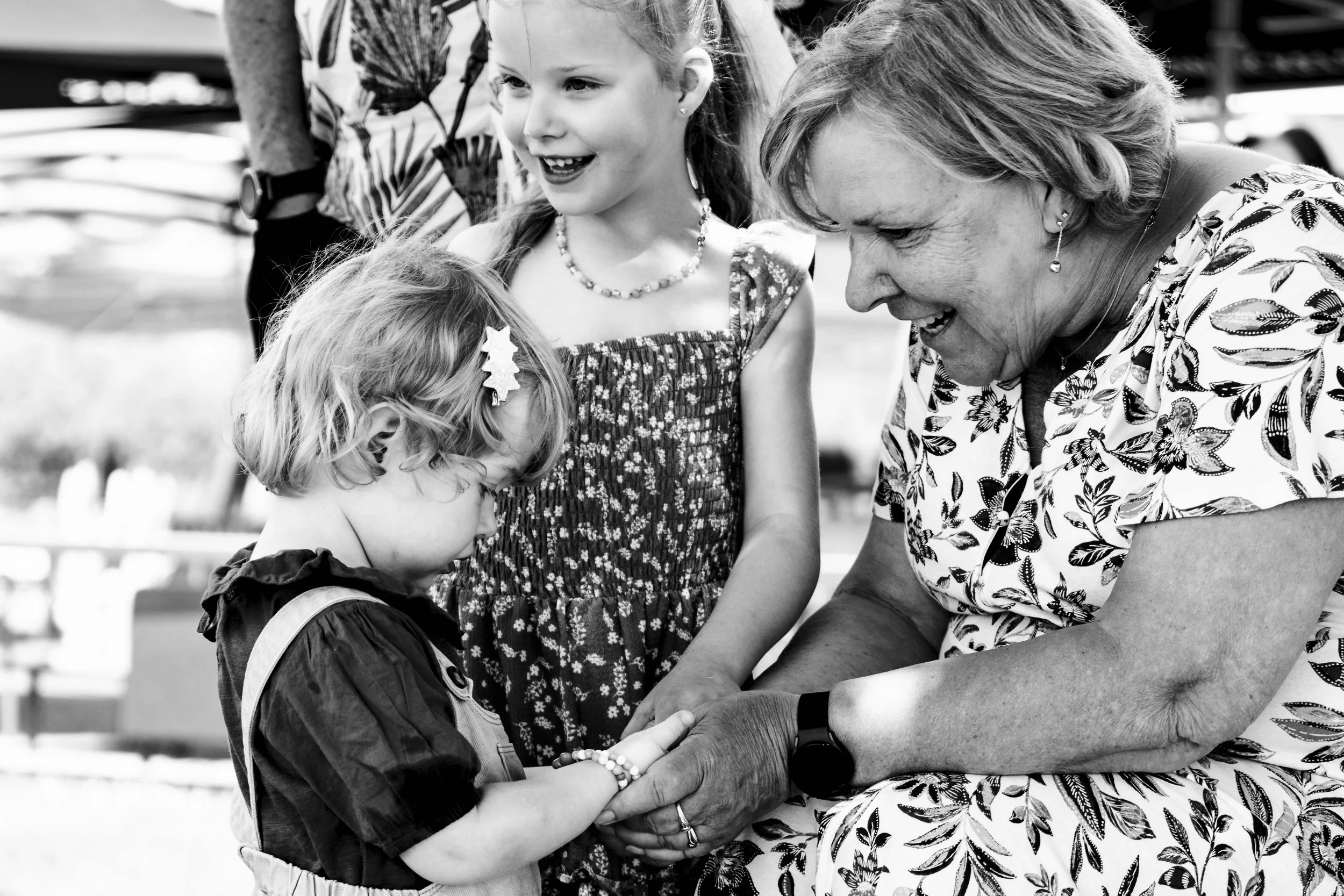 Een oudere vrouw houdt de hand van een jonge meisje vast, terwijl twee andere jonge meisjes toekijken en lachen.