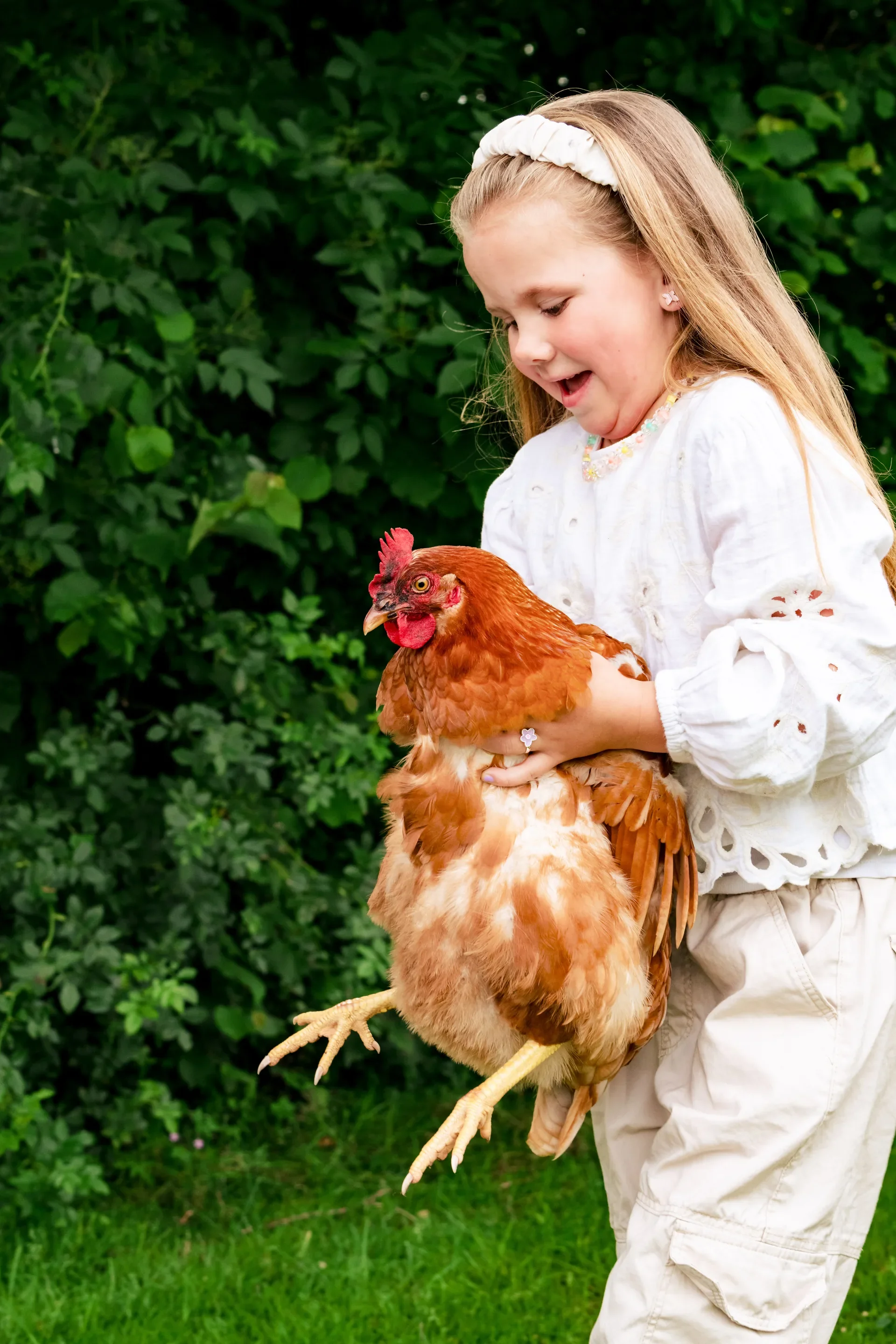 Een jonge meisje houdt een grote kip vast in een groene tuin.