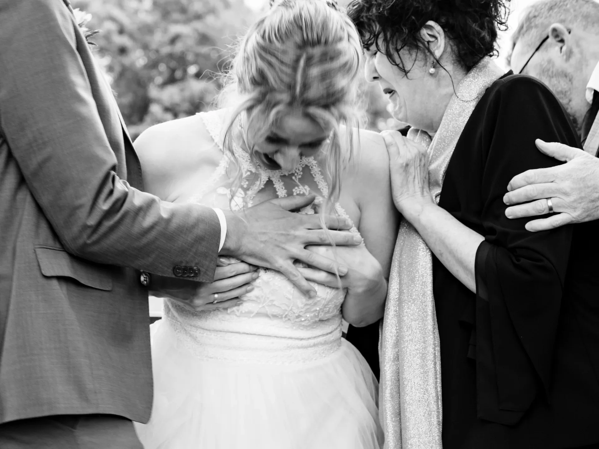 Bruidegom, bruid en familie in emotionele omhelzing tijdens de huwelijksceremonie.