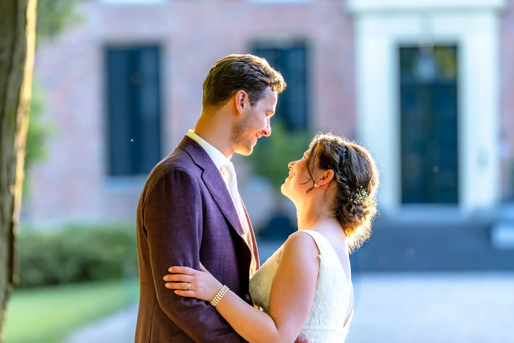 Een koppel houdt elkaar vast en kijkt verliefd naar elkaar in een buitenplaats, mogelijk tijdens een huwelijksceremonie.