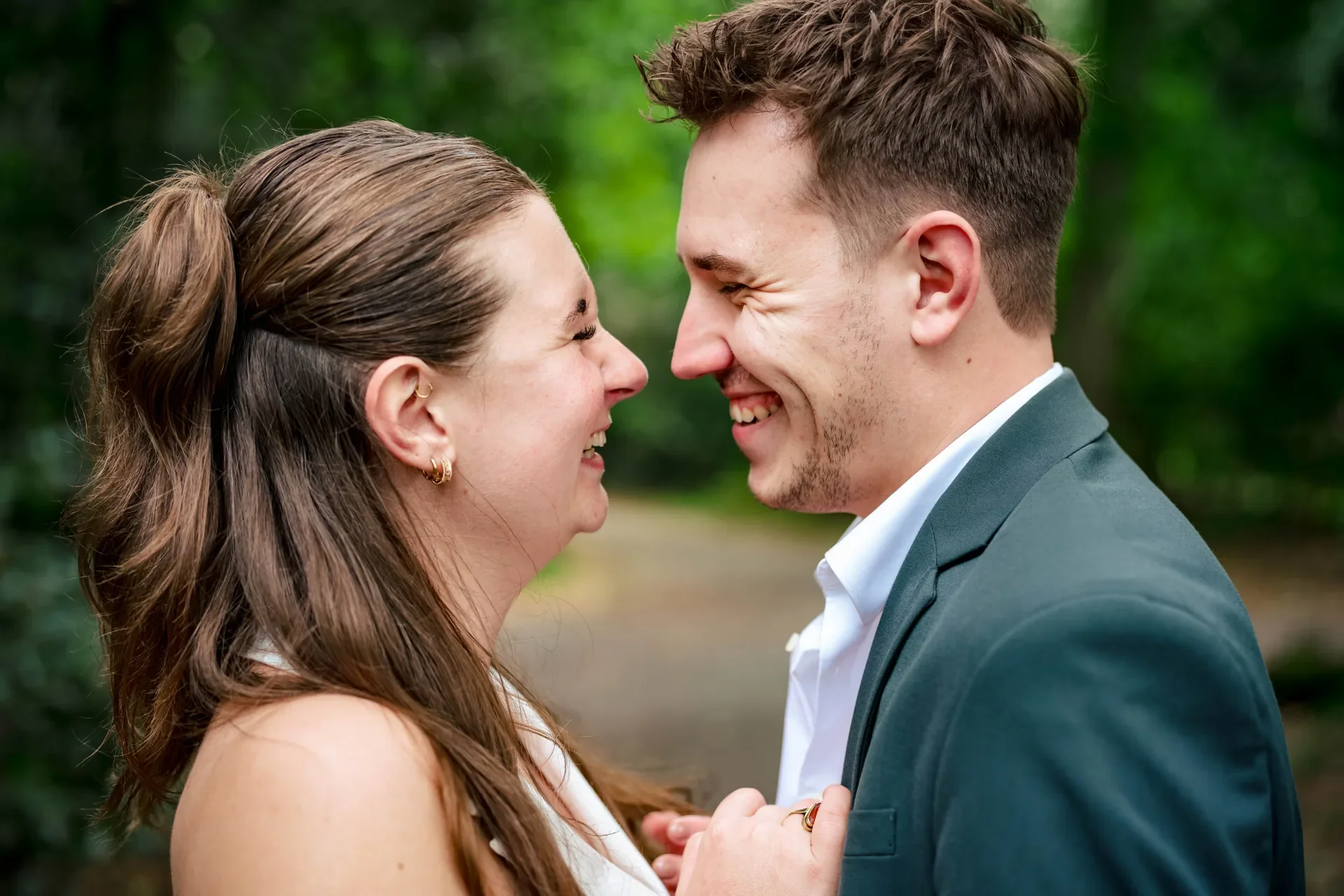 Een stel dat dicht bij elkaar staat, lachend, in een bosrijke omgeving.