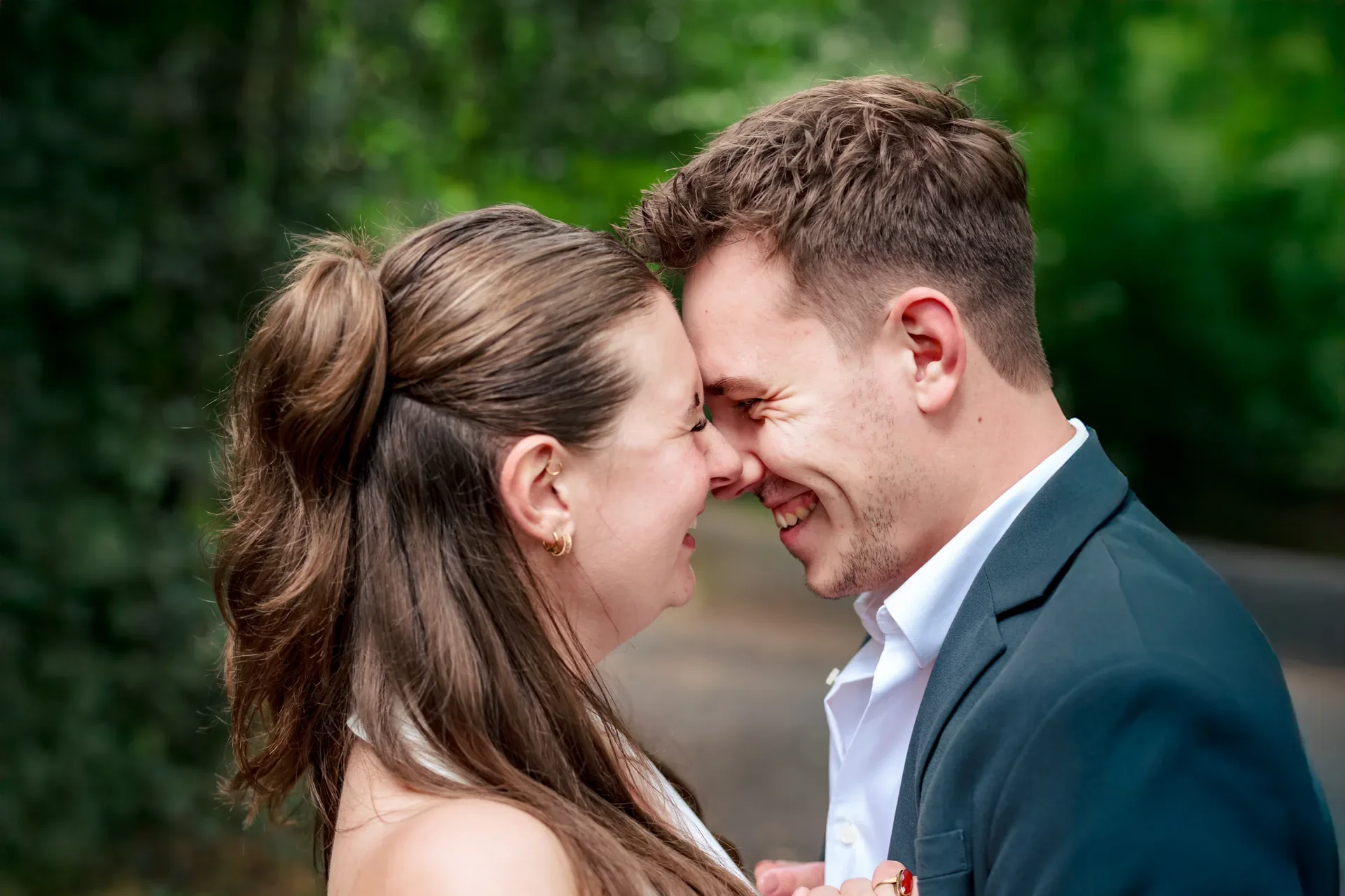 Een stel dat dicht bij elkaar staat, met natte hoofden, glimlachend en elkaar aanraken, buiten met groene bladeren op de achtergrond.