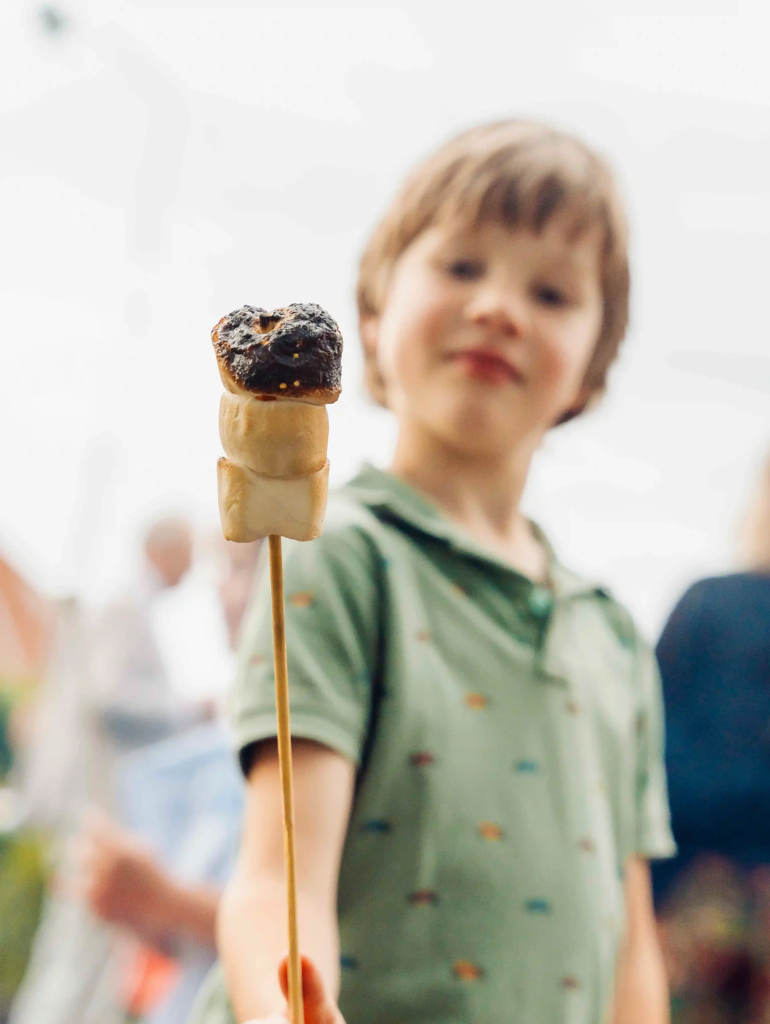 Een kind houdt een spies met een marshmallow en een geroosterde vrucht, mogelijk een persimmon of haselnuss, voor de camera.