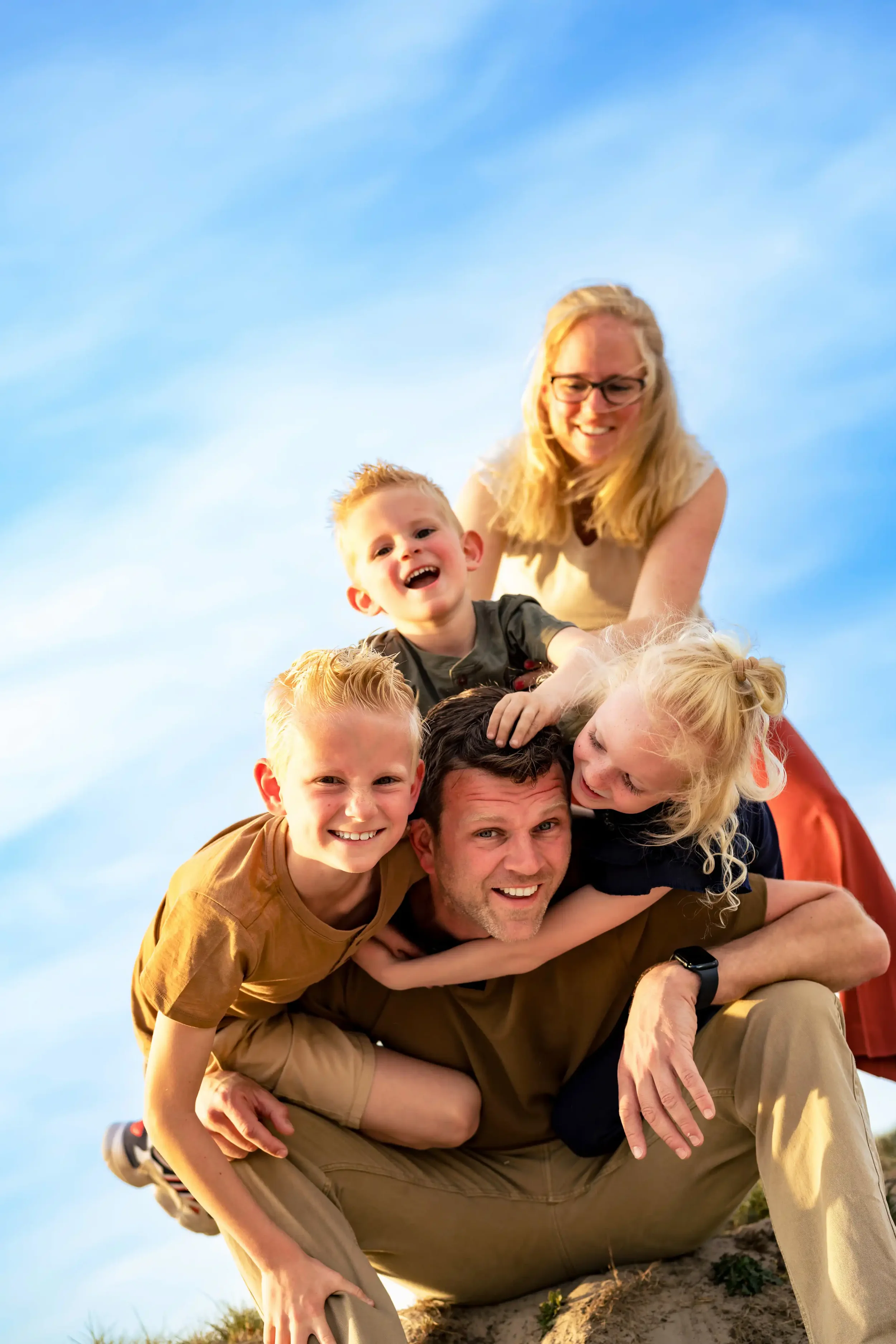 Familie speelt samen op een zandheuvel onder een blauwe hemel.