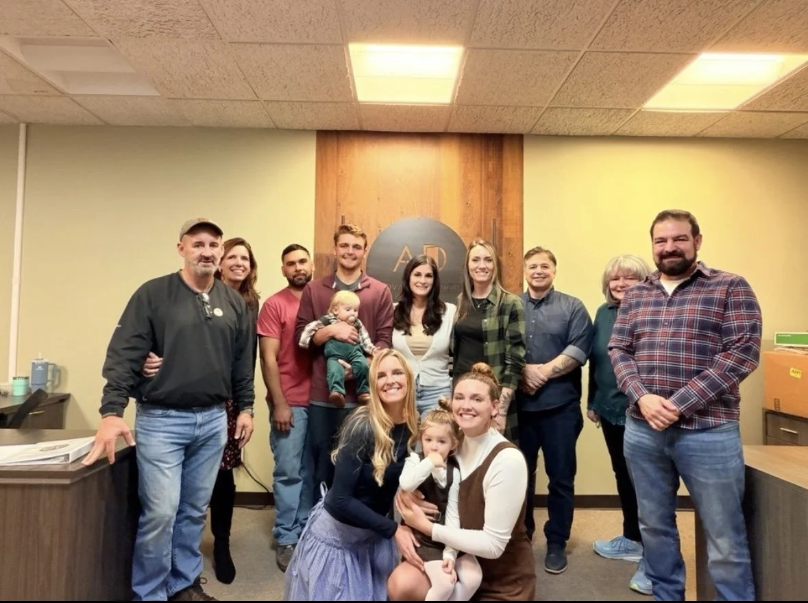 Group of people smiling in a room with a wooden wall and a sign that says 'AD' in the background.