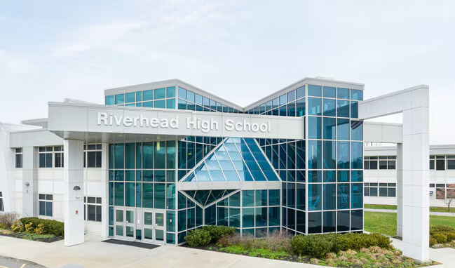 Exterior of Riverhead High School with modern glass and white building design.