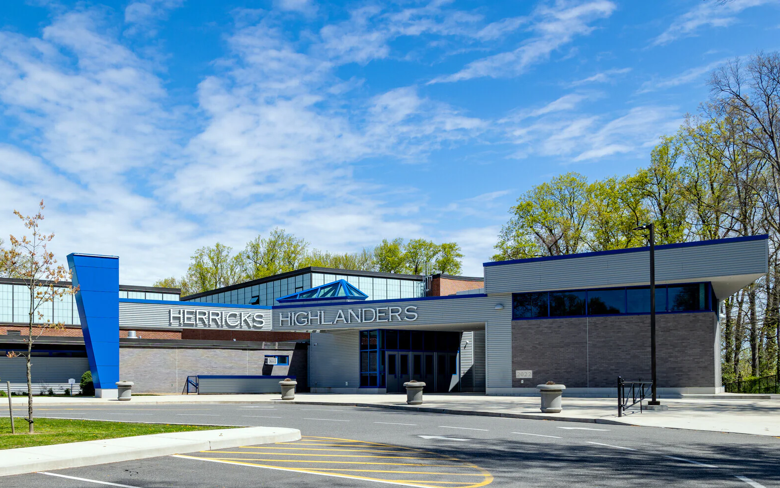 Front entrance of Herricks Highlanders school with modern architecture, blue accents, and a partly cloudy sky