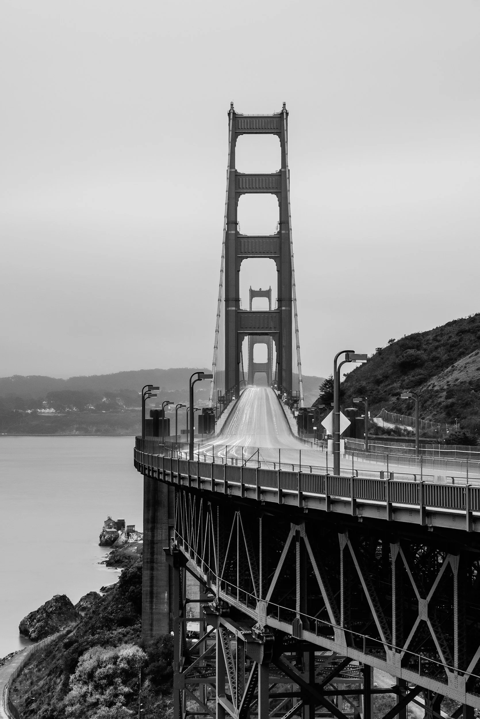 Black and white photo of the Golden Gate Bridge with no vehicles or pedestrians, showing its towers and suspension cables over water with hills in the background. For the Founder of B-Rad HQ, this symbolizes the structure of his mission.
